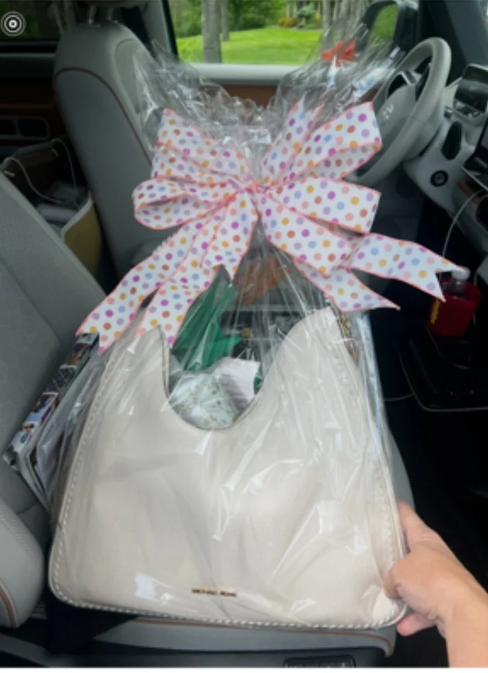 A large gift basket wrapped in clear plastic with a colorful polka dot bow, held on the seat of a vehicle.