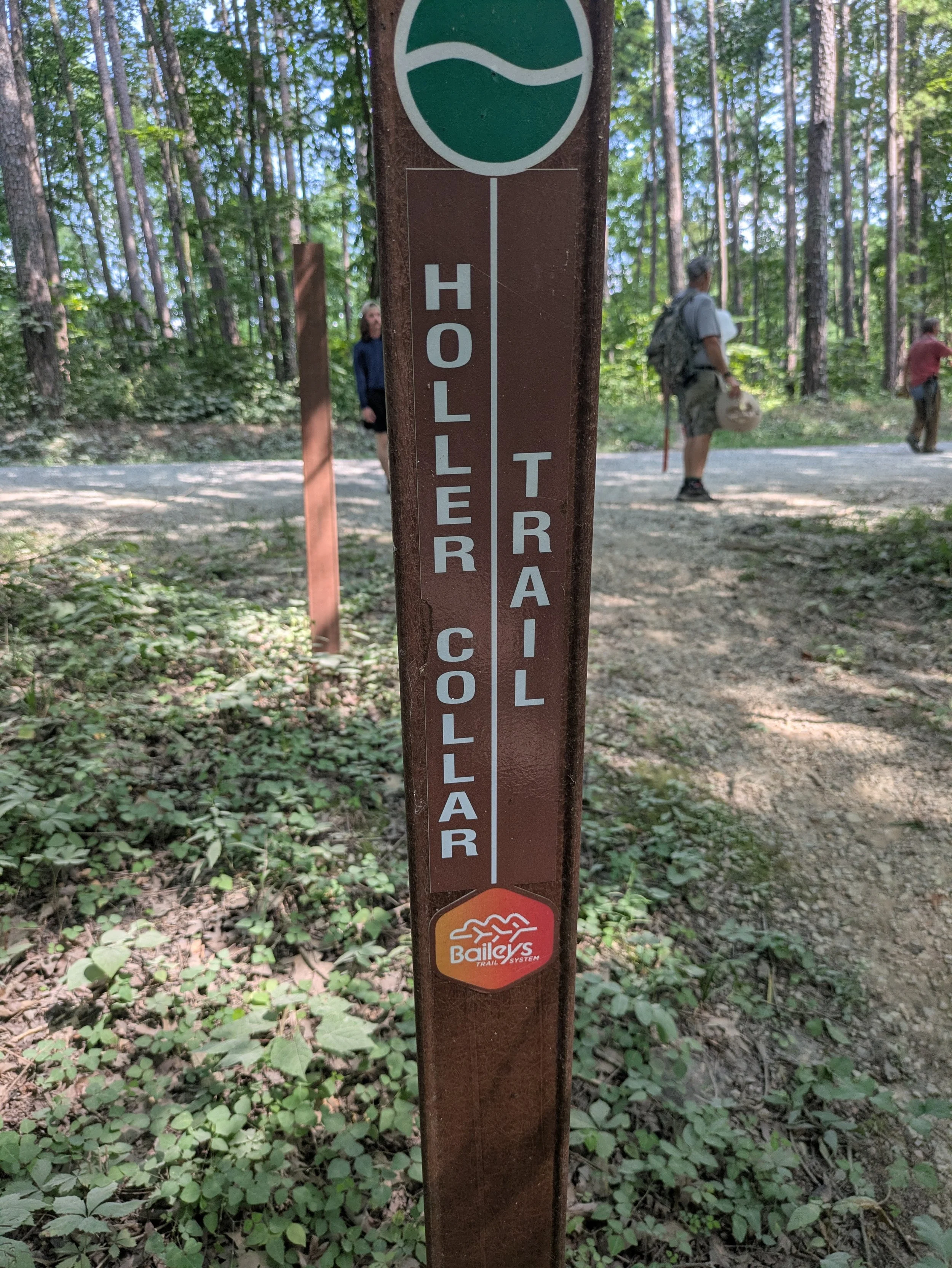 Trail sign in a forest indicating a trail closure, with a small Bale's Trail System logo at the bottom, surrounded by trees and green foliage.