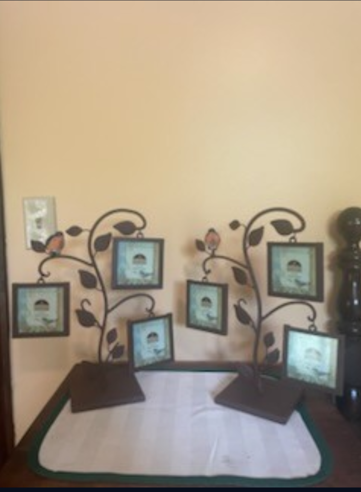 Decorative photo display with framed images hanging on black metal branches, placed on a table against a beige wall.