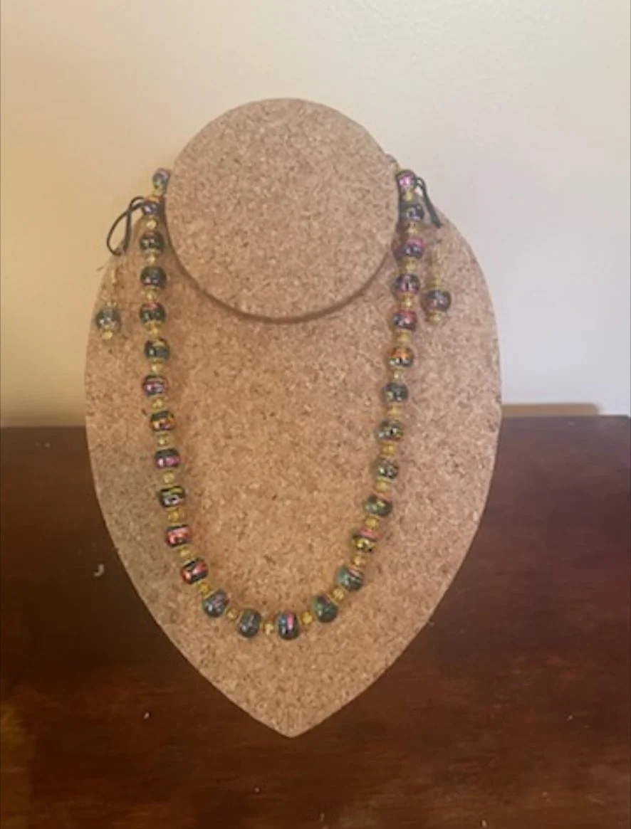 Beaded necklace with multicolored beads displayed on a cork jewelry stand on a wooden surface.