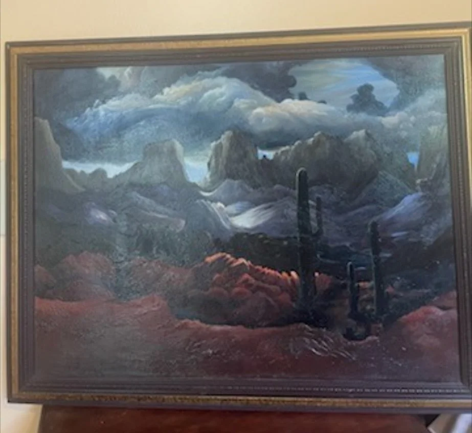 A landscape painting of a desert scene with mountains, some cacti, and dark storm clouds in the sky.