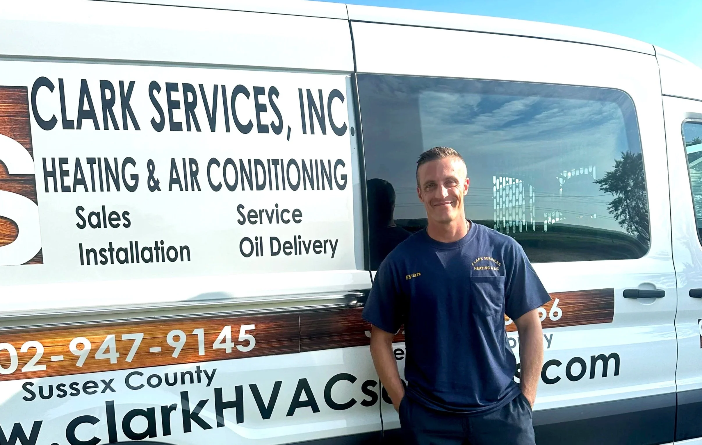 A man with short, light brown hair and a trimmed beard, wearing a beige and brown plaid shirt, standing indoors with a slight smile.