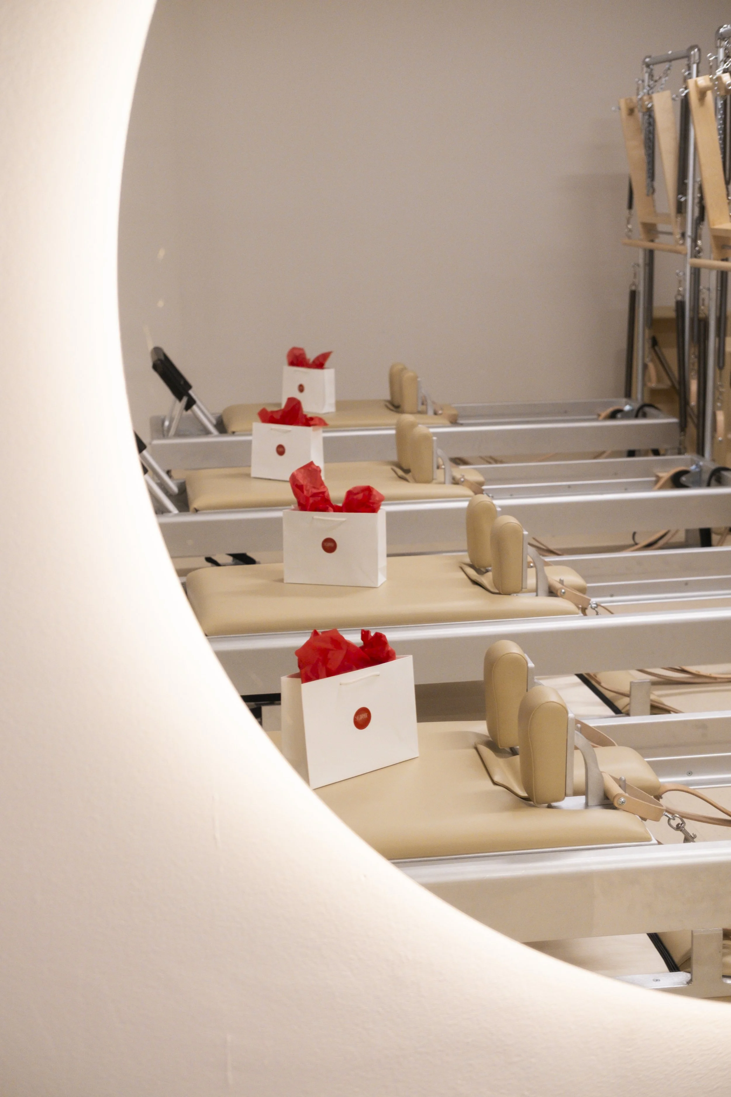 Multiple hospital or medical beds lined up in a row in a clinical setting, with white boxes and red tissue paper on each. The image is partially framed by a white wall or curtain in the foreground.