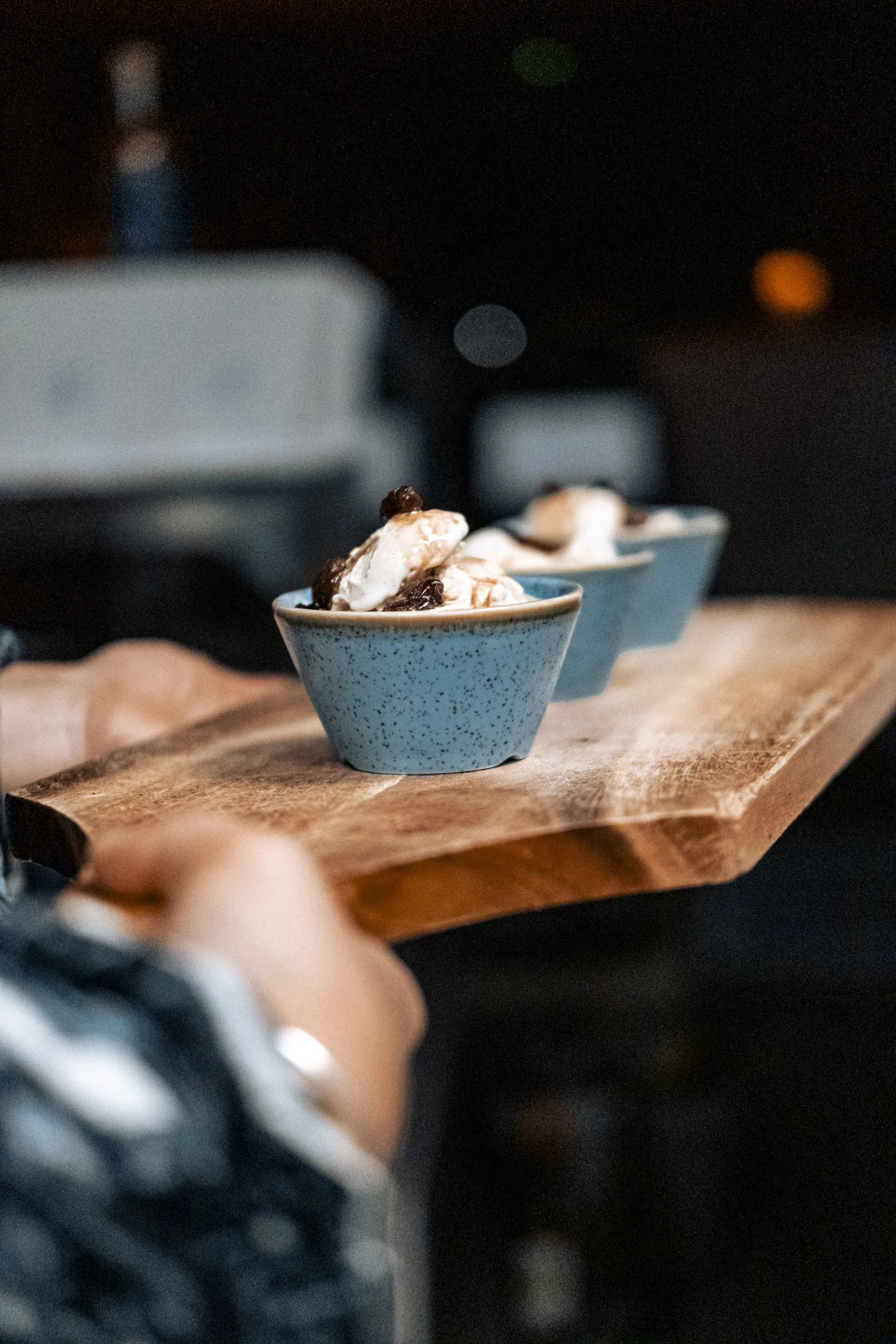 Close-up of three small blue bowls filled with a dessert that appears to have whipped cream and chocolate, placed on a wooden serving board.
