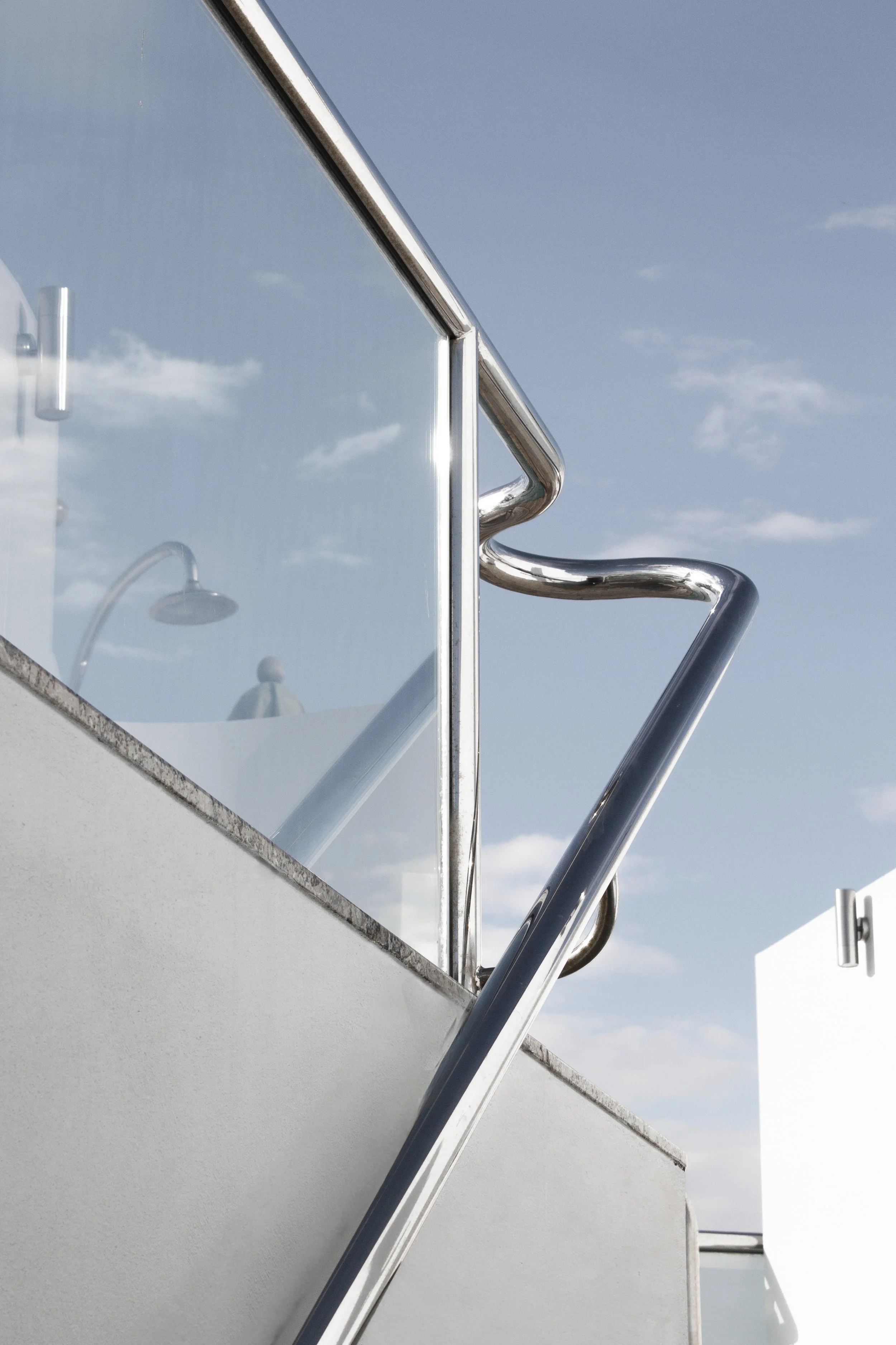 Close-up of metal handrails on a boat or yacht, with a mirror-like reflection showing parts of the boat's structure against a blue sky with a few clouds.