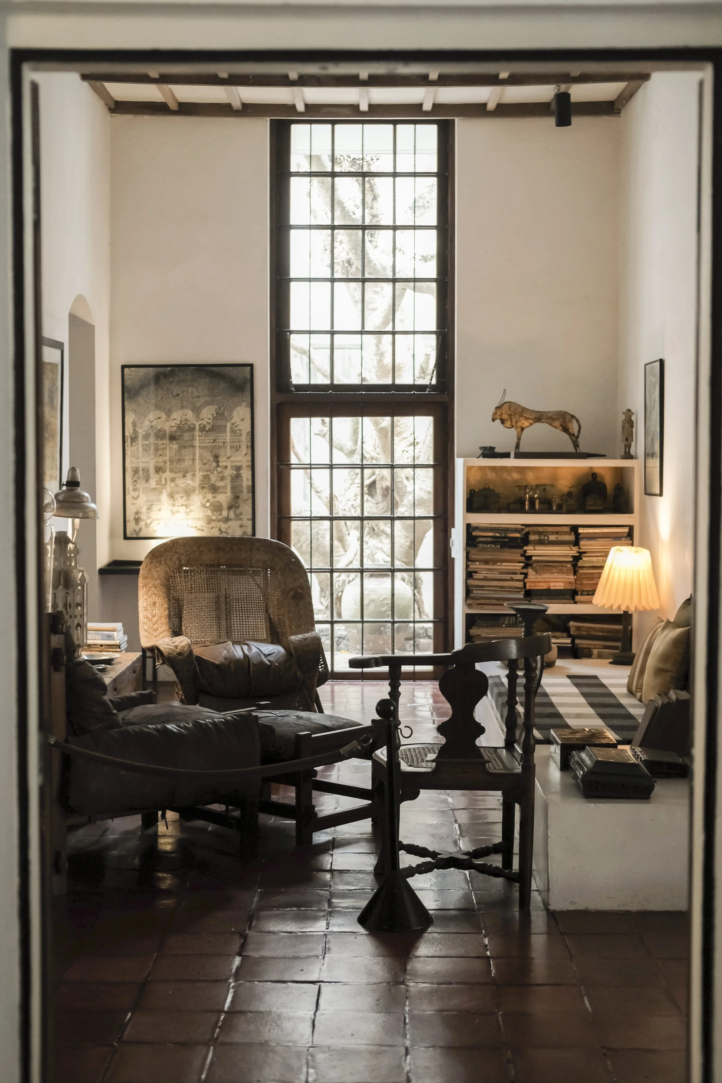 Living room with wooden furniture, artwork, large window, and decorative items, including a lion sculpture and a bookshelf.