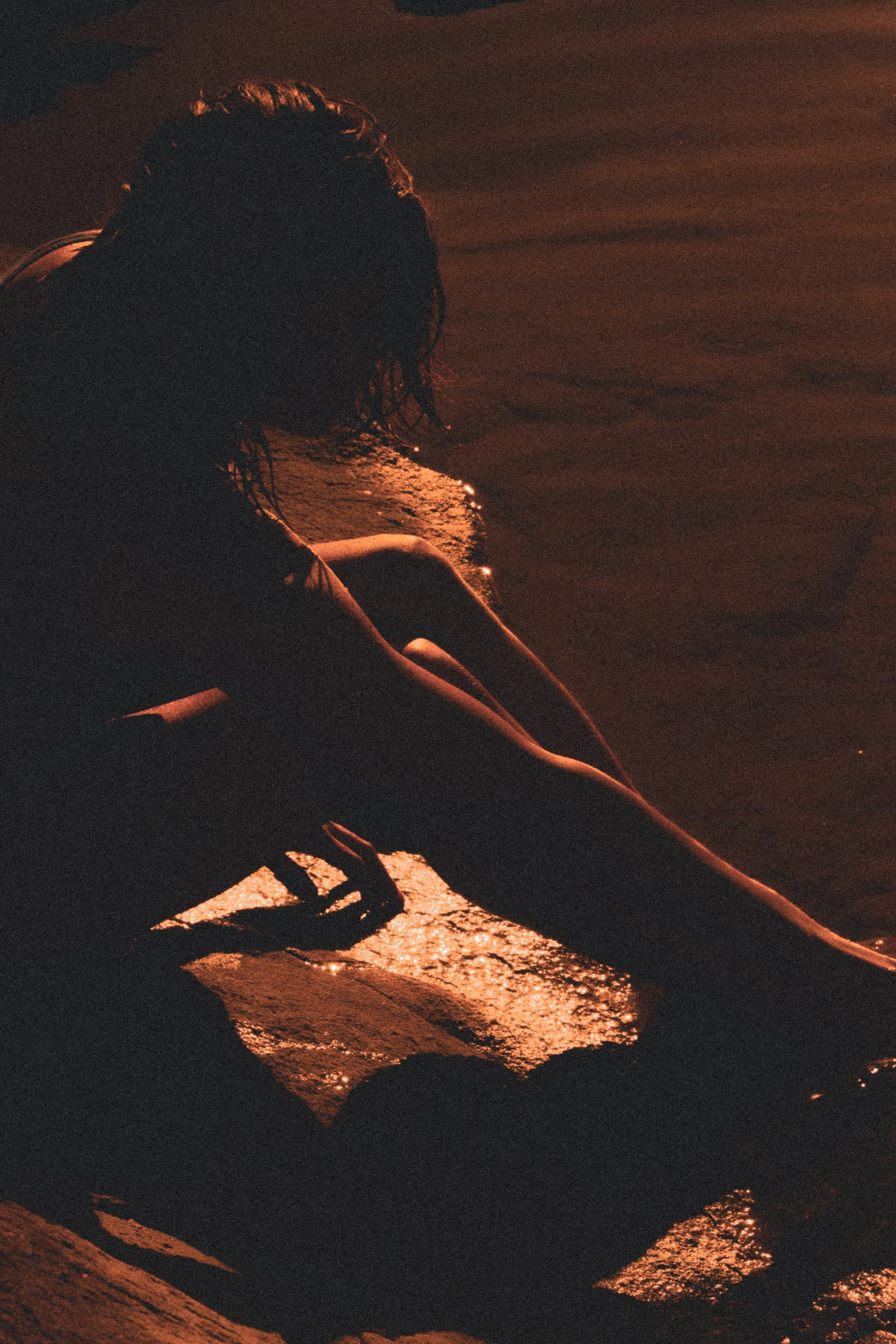 Person sitting by the water at sunset, with reflections of the sunset on the water's surface.