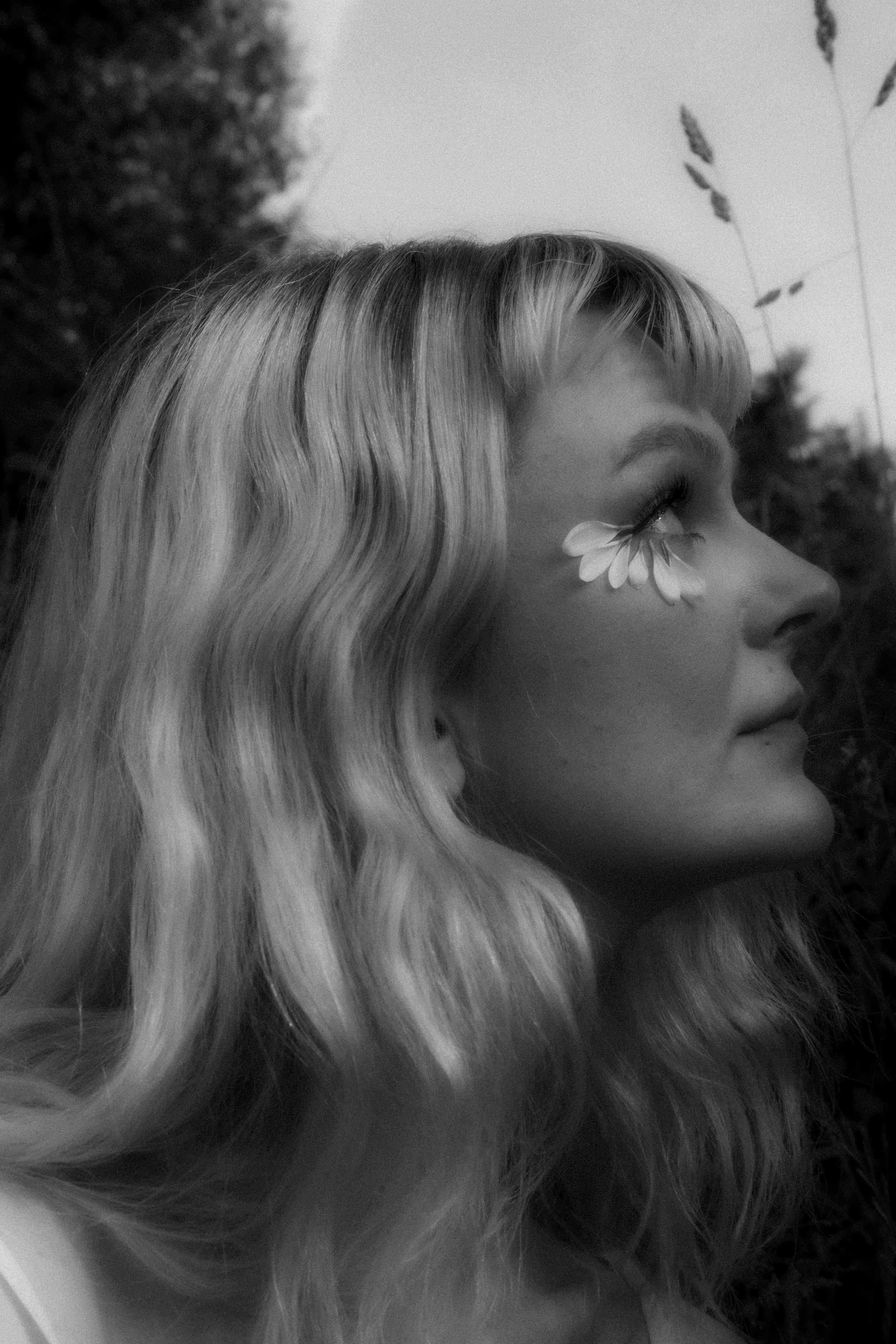 Black and white portrait of a woman with long wavy hair and a flower-shaped face tattoo near her eye, in profile view.