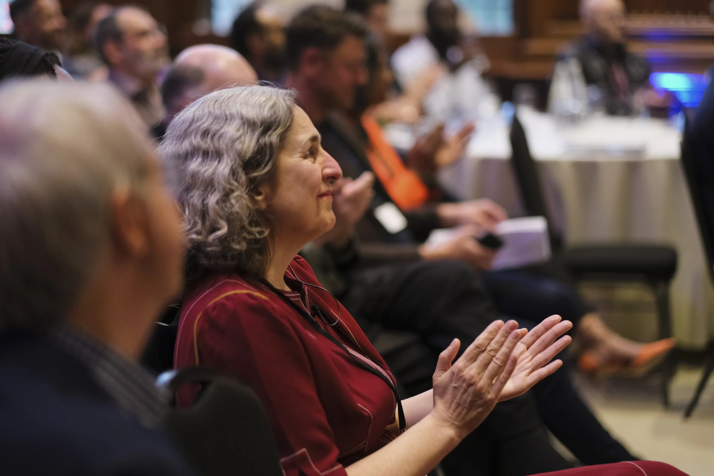 A diverse group of people attentively listening and clapping at a formal event or conference in a banquet hall.
