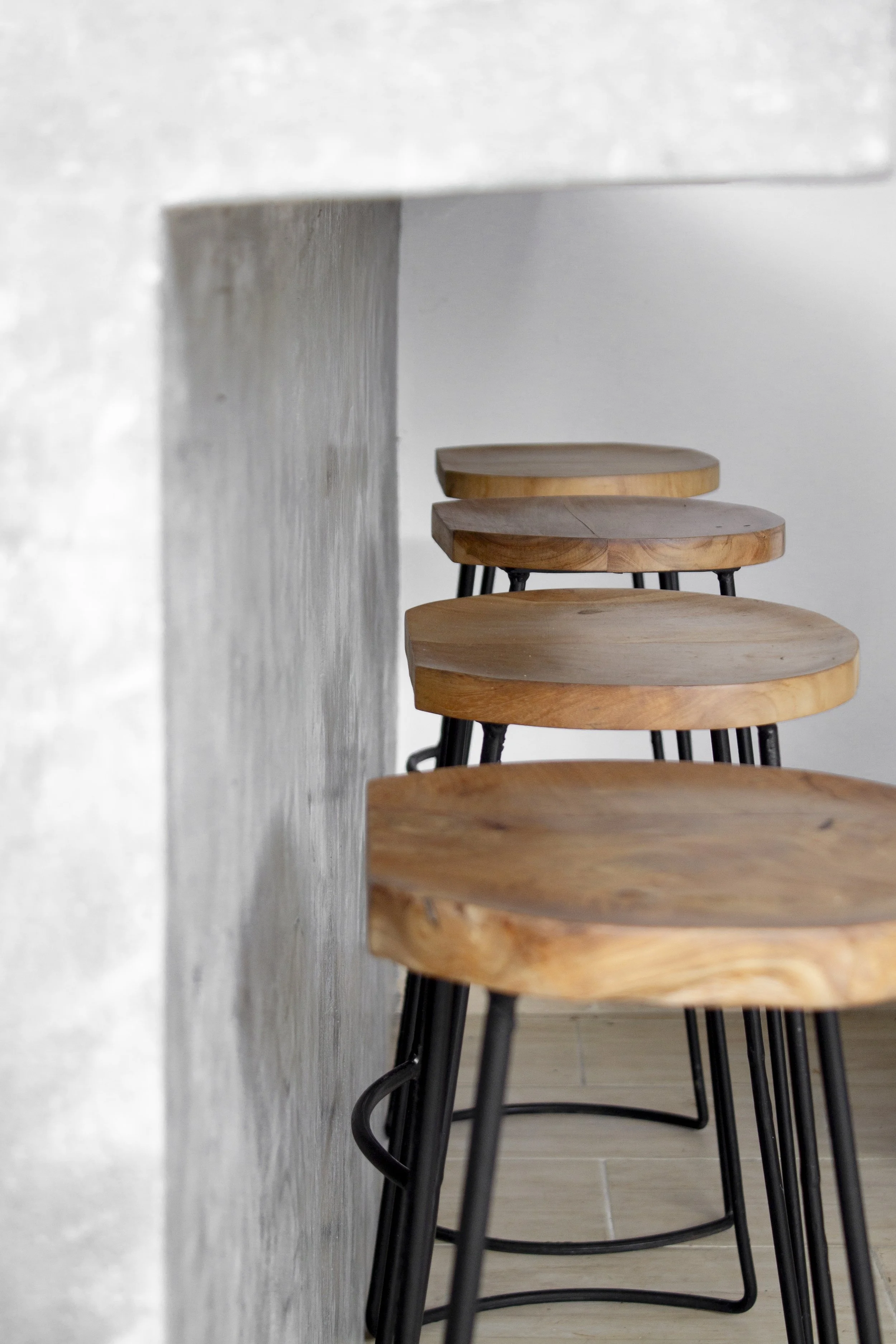 A row of wooden bar stools with black metal legs lined up beside a white wall. The stools have round wooden seats with natural wood grain.