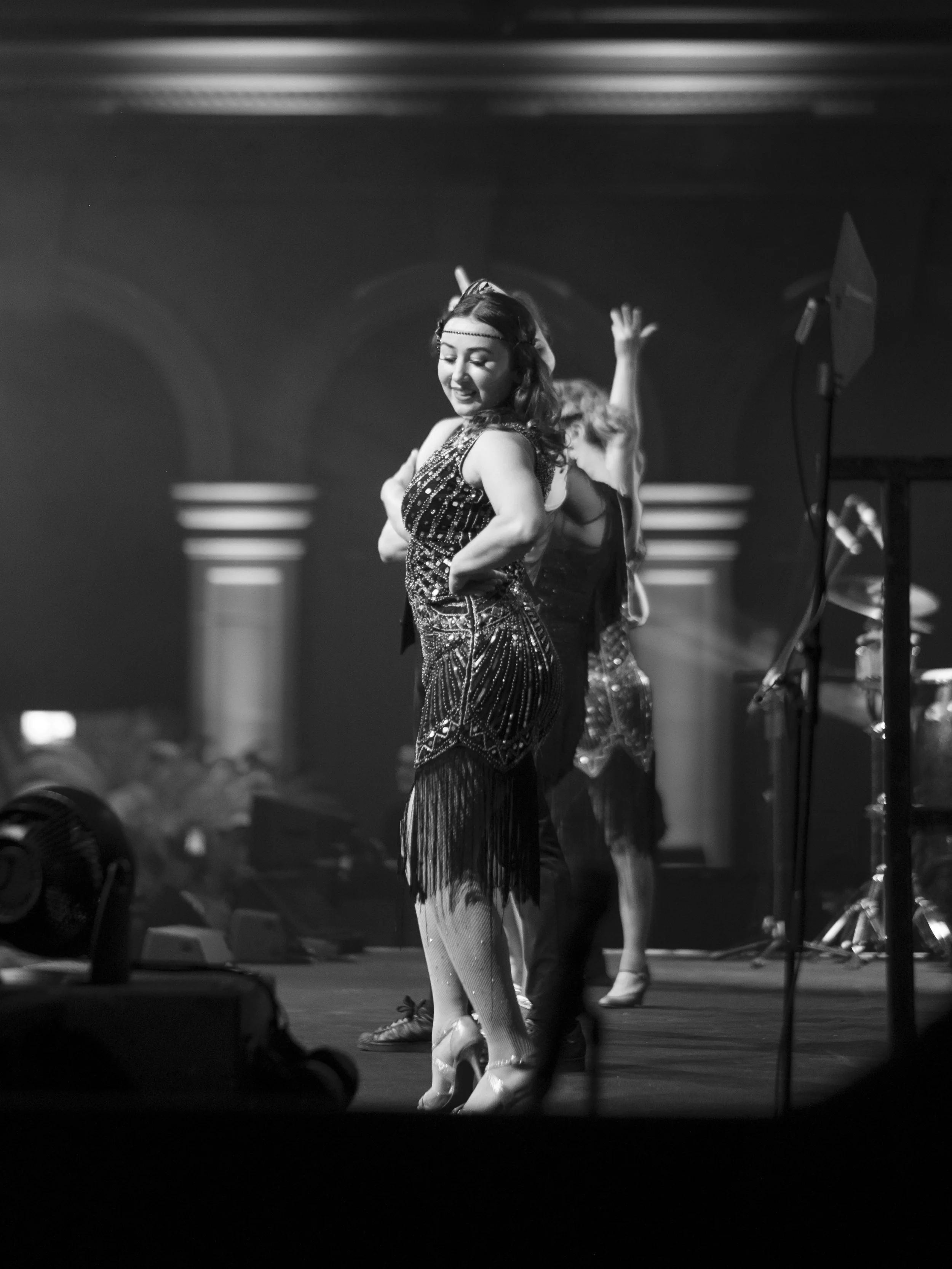 Black and white photo of a female dancer in costume performing on stage with other dancers in the background.