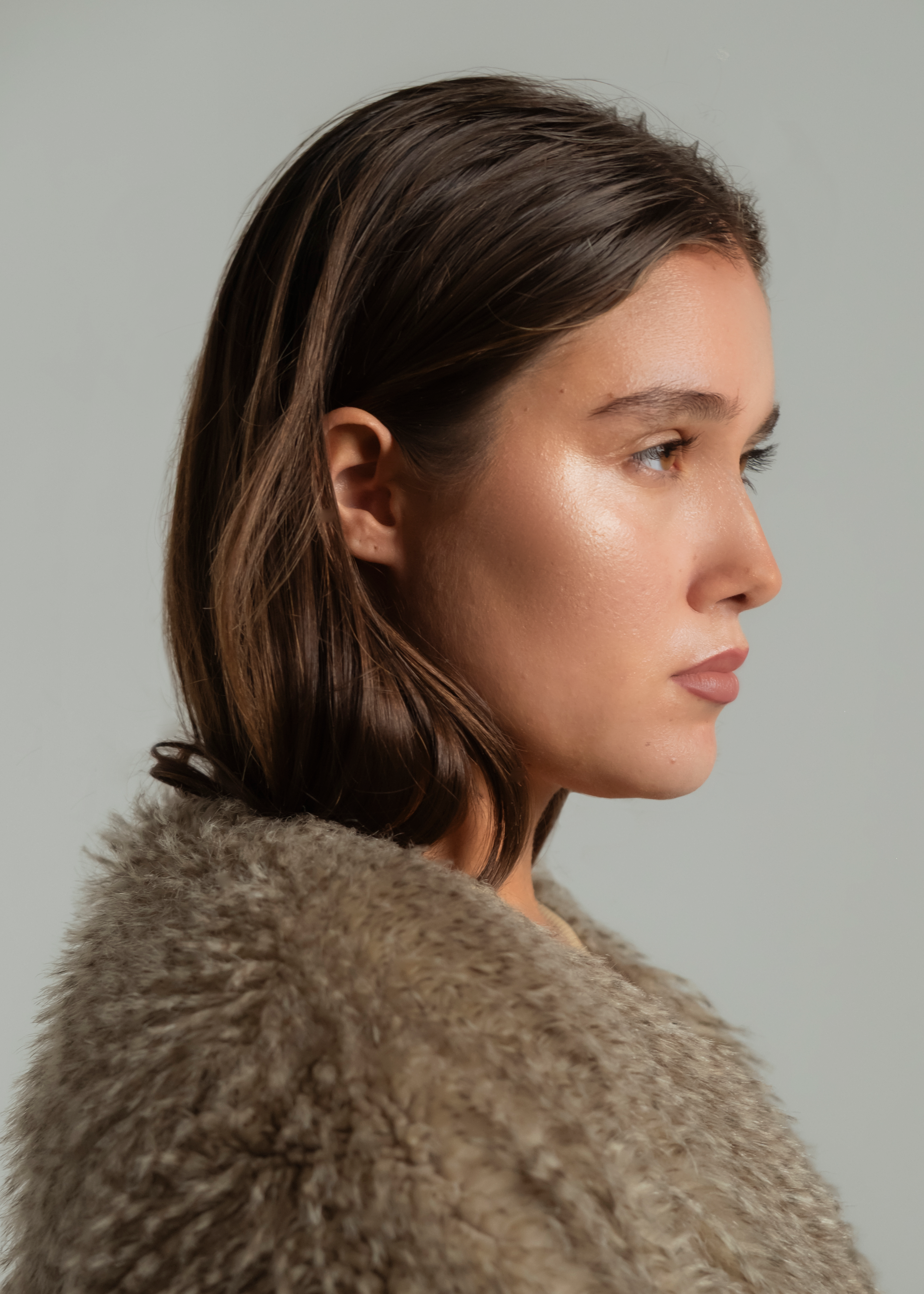 Profile of a young woman with brown hair wearing a beige fur coat.