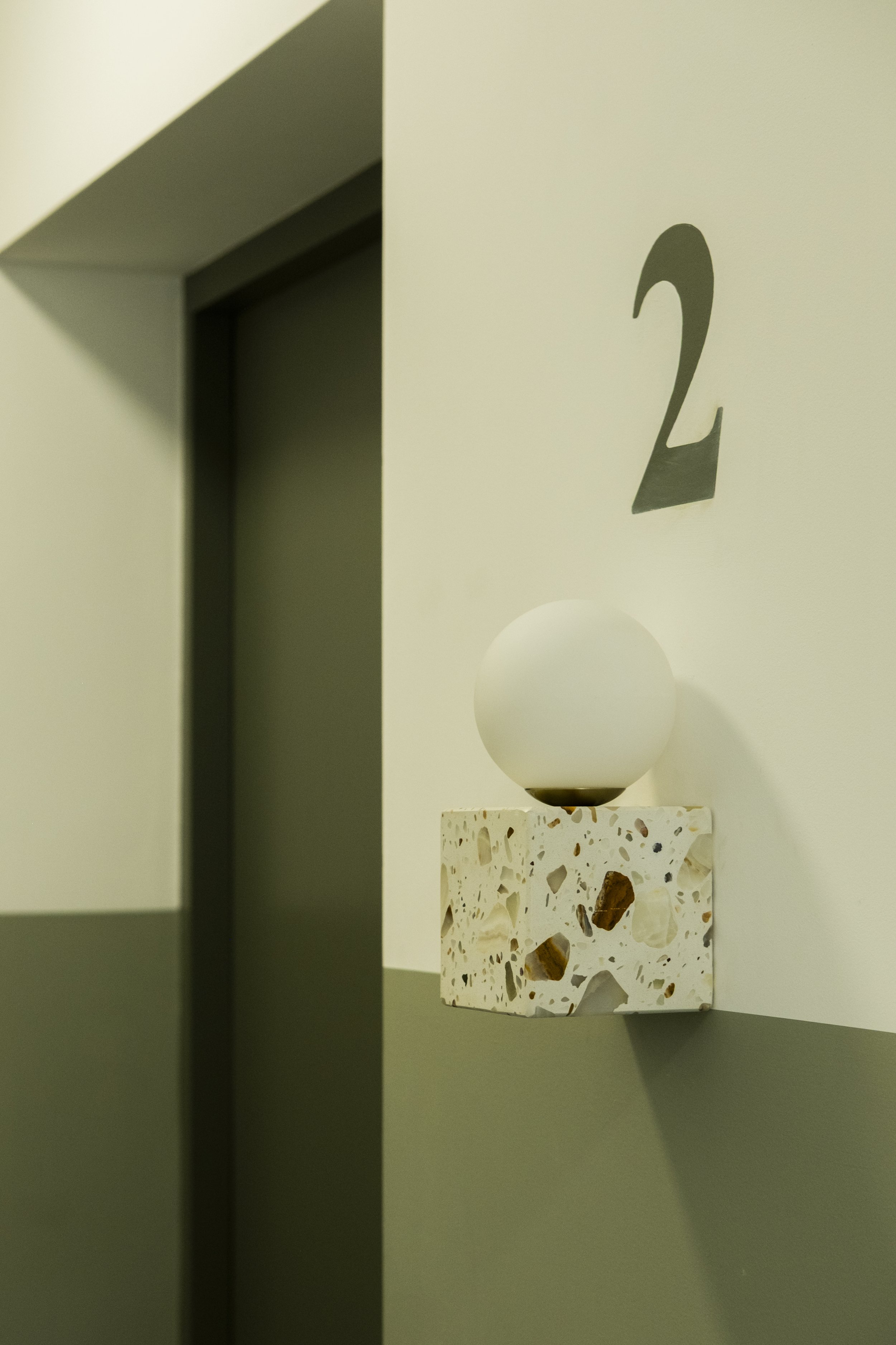 Close-up of a modern decorative lamp with a frosted globe sitting on a terrazzo base, and a wall with a large black number 2 beside it.