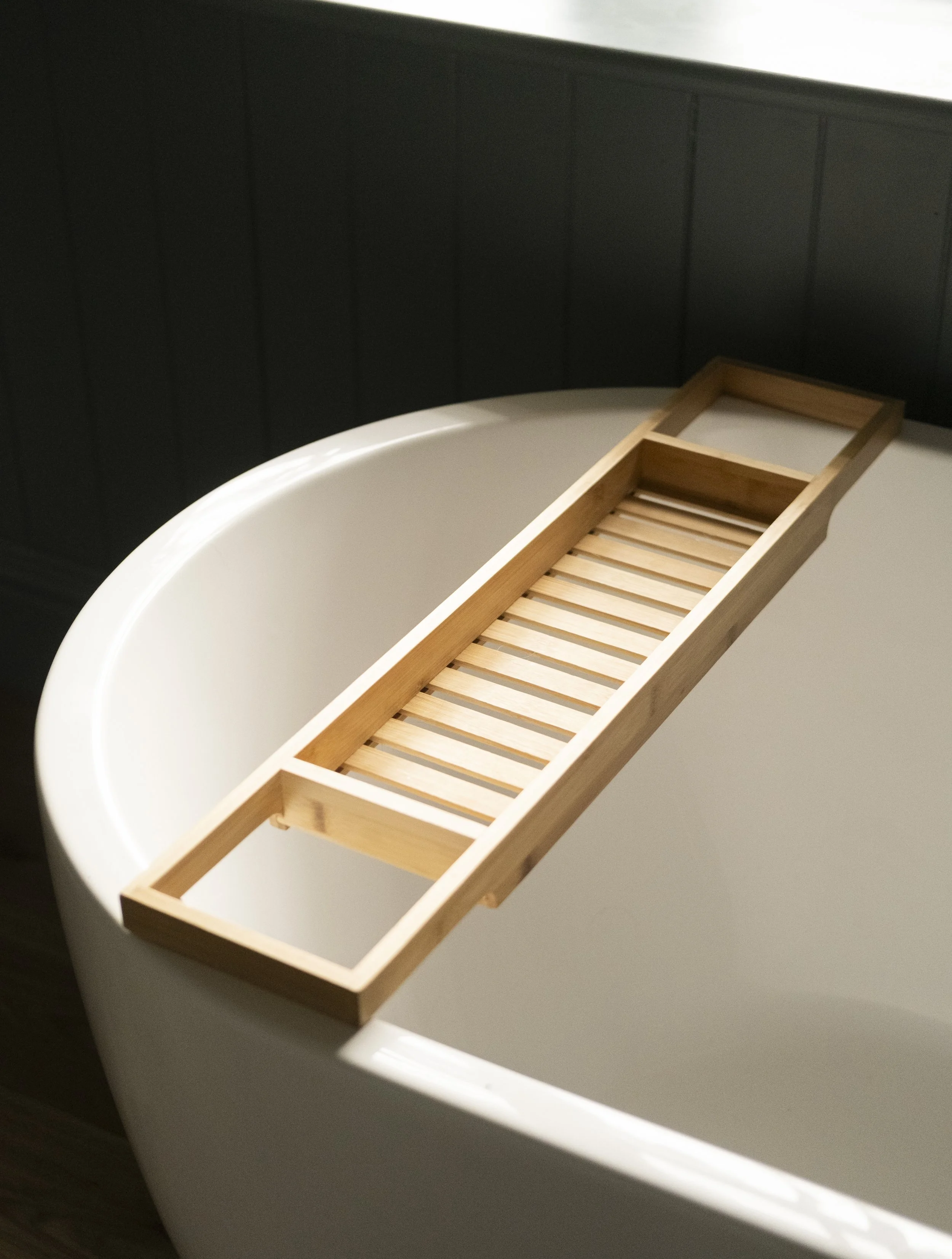 A white bathtub with a wooden bath caddy placed on its edge.