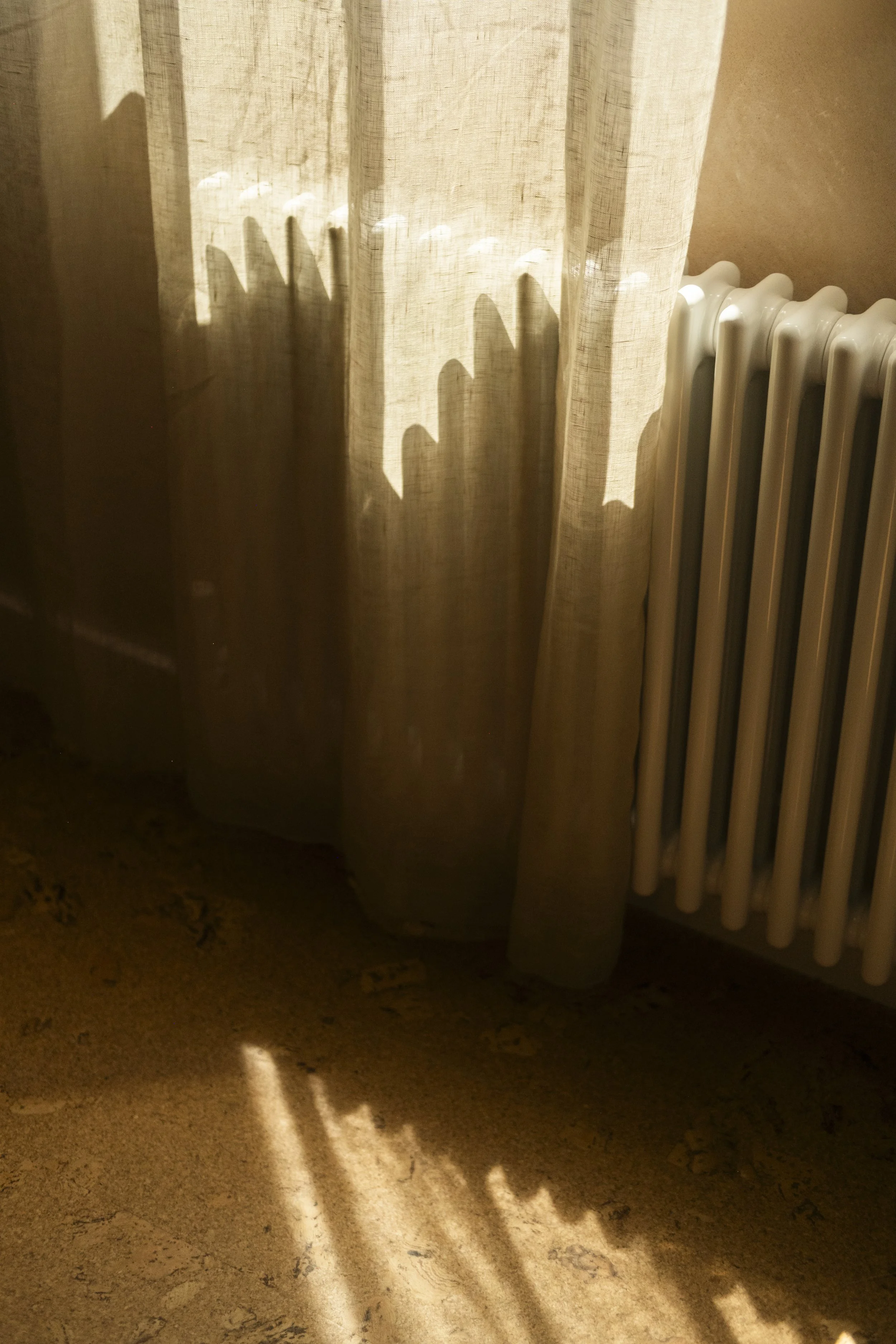 Sunlight creates shadows of a curtain and radiator on a textured floor.