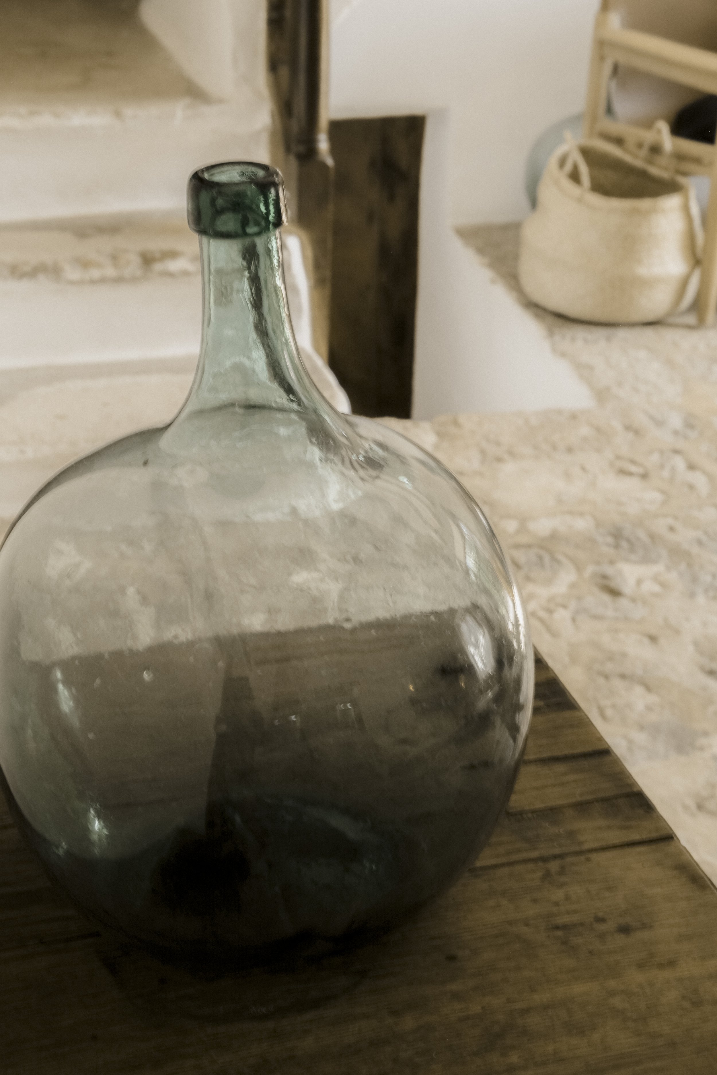 Close-up of a clear glass bottle with a dark liquid inside, placed on a wooden surface in a cozy kitchen setting.