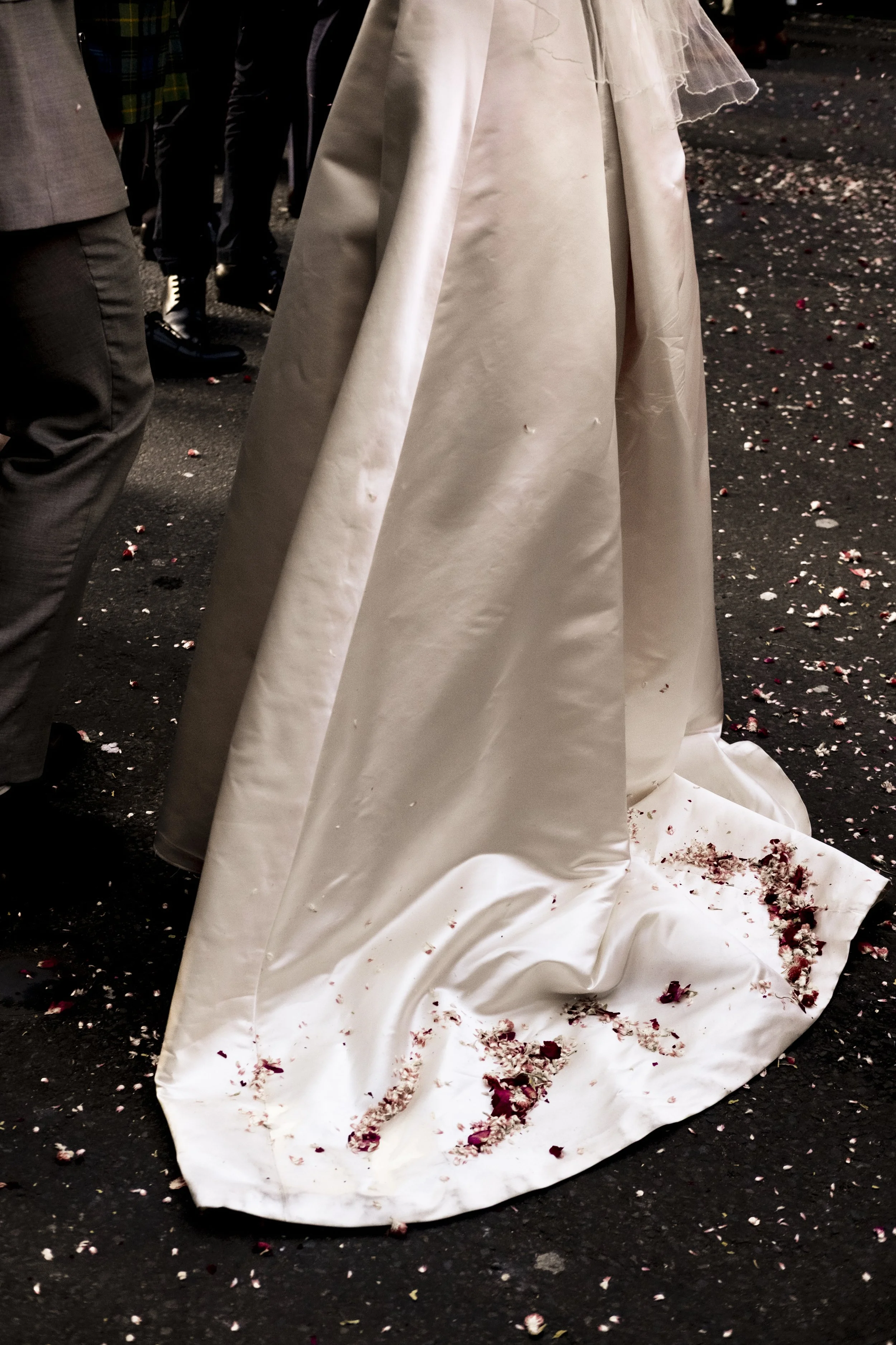 A white wedding dress on the floor with bloodstains and flower petals around it on a dark ground.