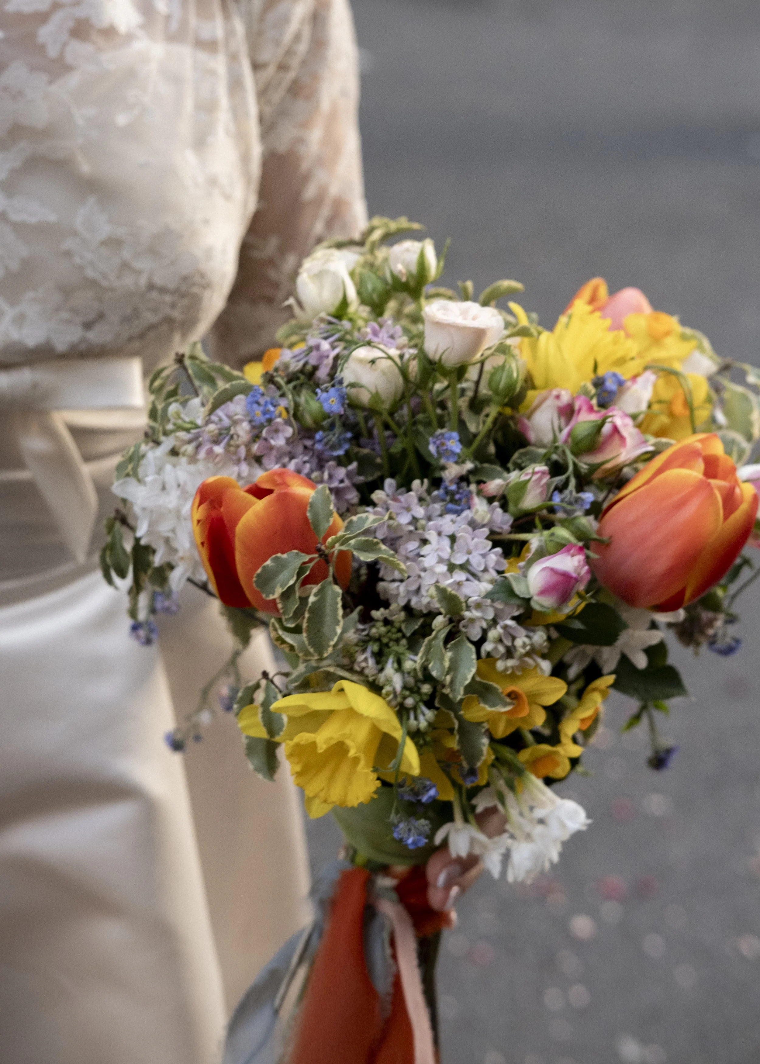 A person holding a colorful bouquet of flowers, including white, yellow, orange, pink, and purple blooms.
