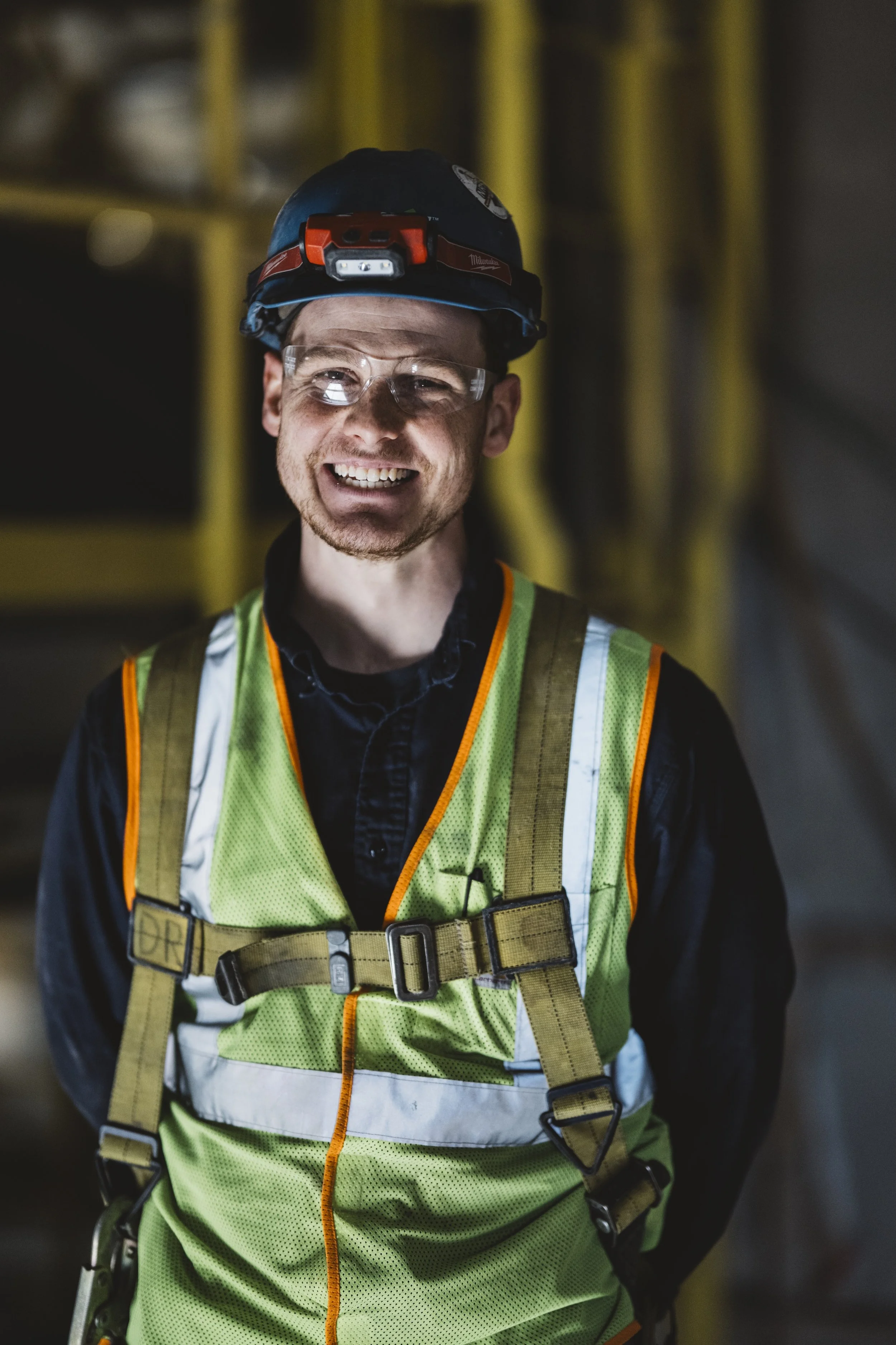 A smiling construction worker in a safety vest and helmet at a construction site.