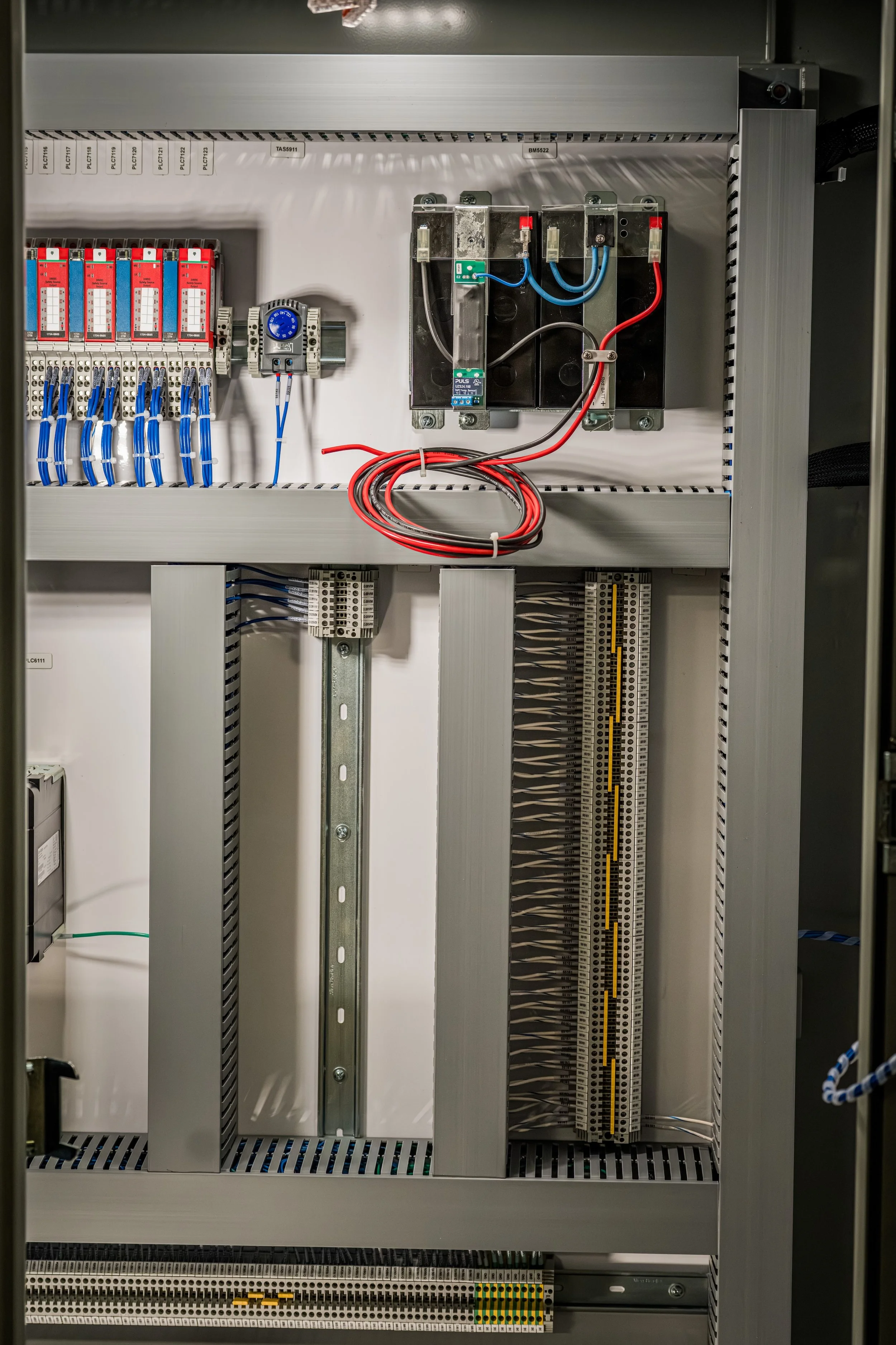 Inside an electrical control panel with wiring, relays, terminal blocks, and circuit breakers.
