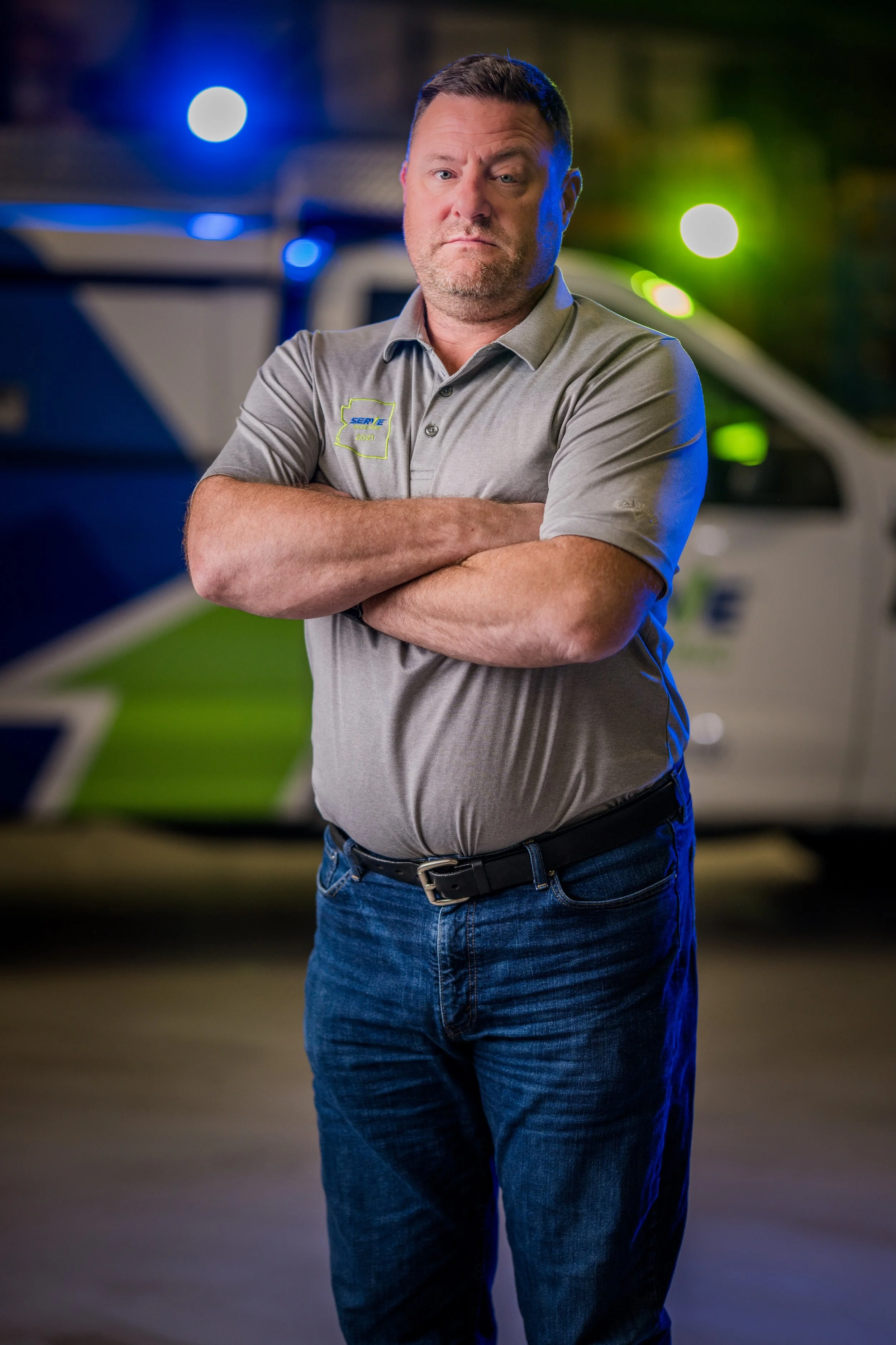 Man with crossed arms standing in front of police or emergency vehicle at night
