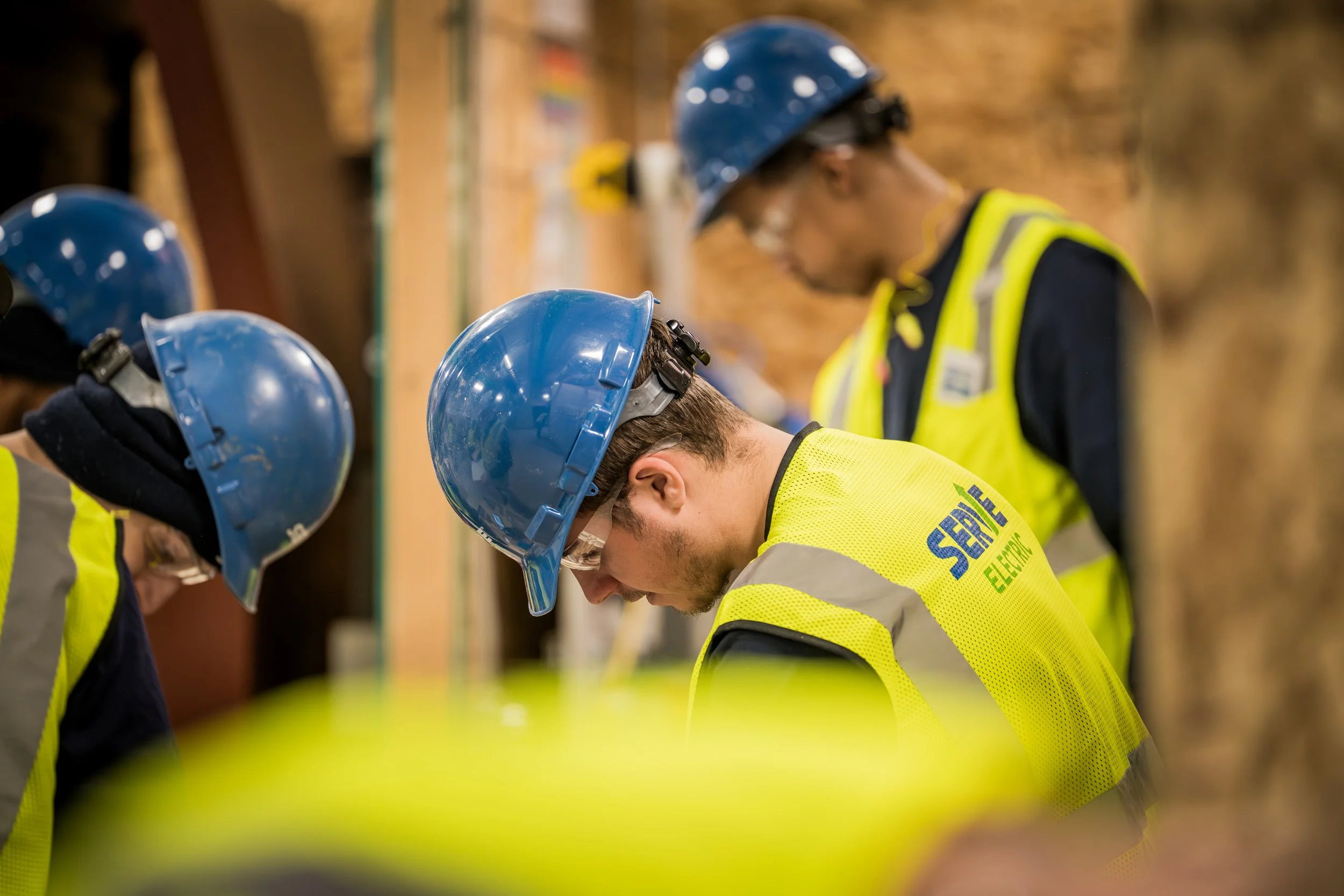 Construction workers wearing blue safety helmets and neon yellow safety vests, working closely together at a construction site.