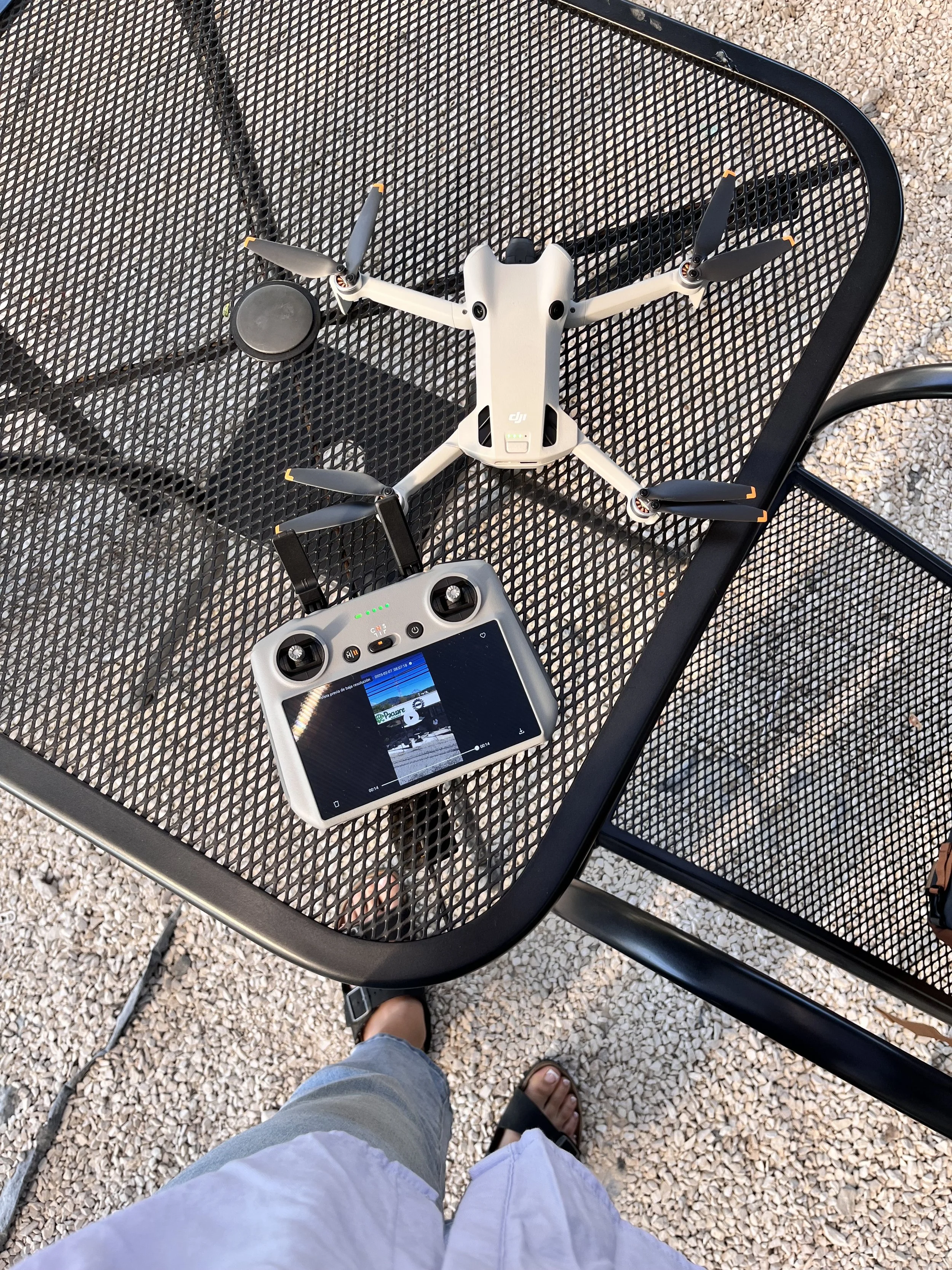 Dron con cámara y controlador sobre mesa de metal con vista al suelo de piedra.