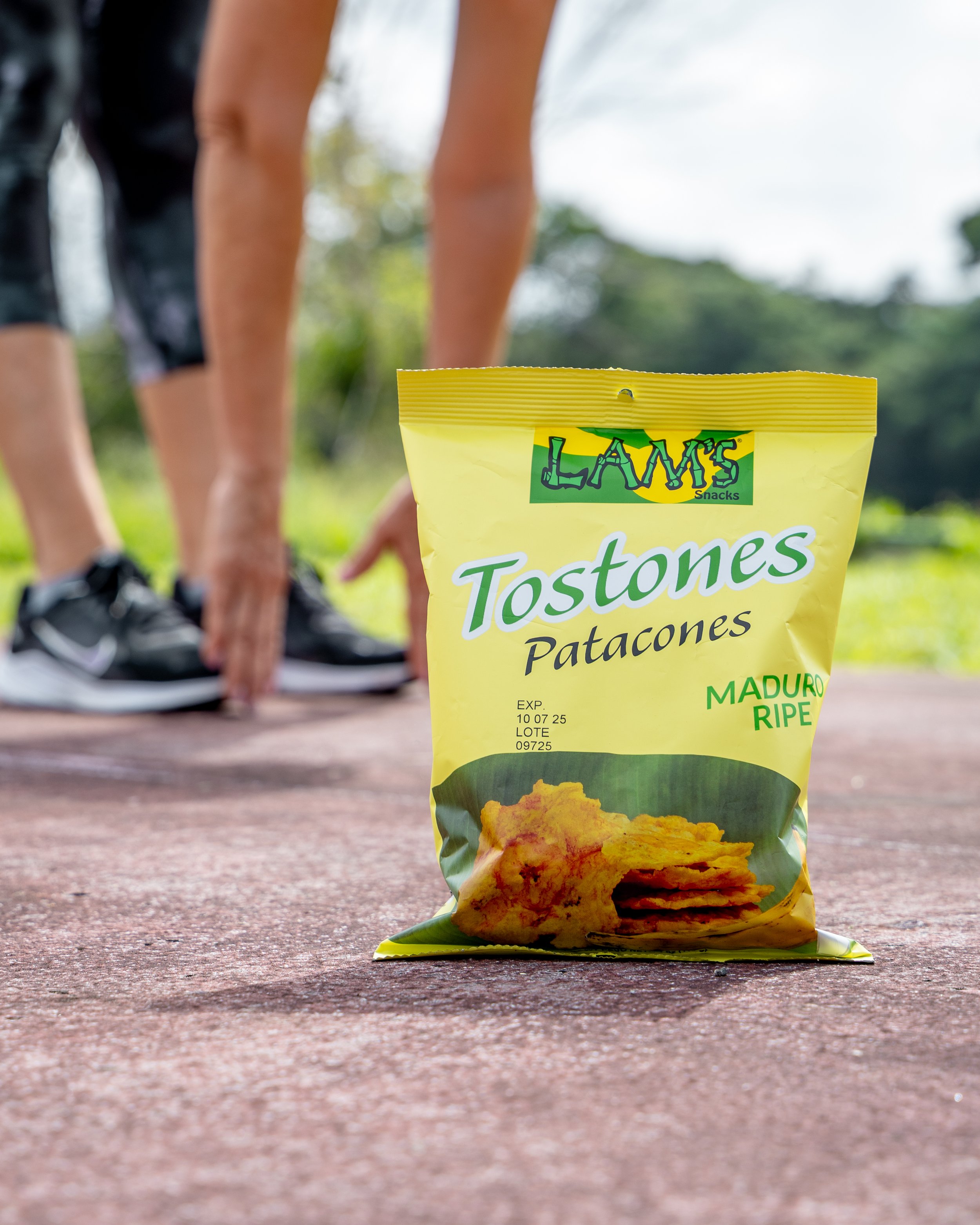 Paquete de tostadones de papas fritas en primer plano en una superficie de madera, con una persona haciendo ejercicio al fondo en un entorno al aire libre.