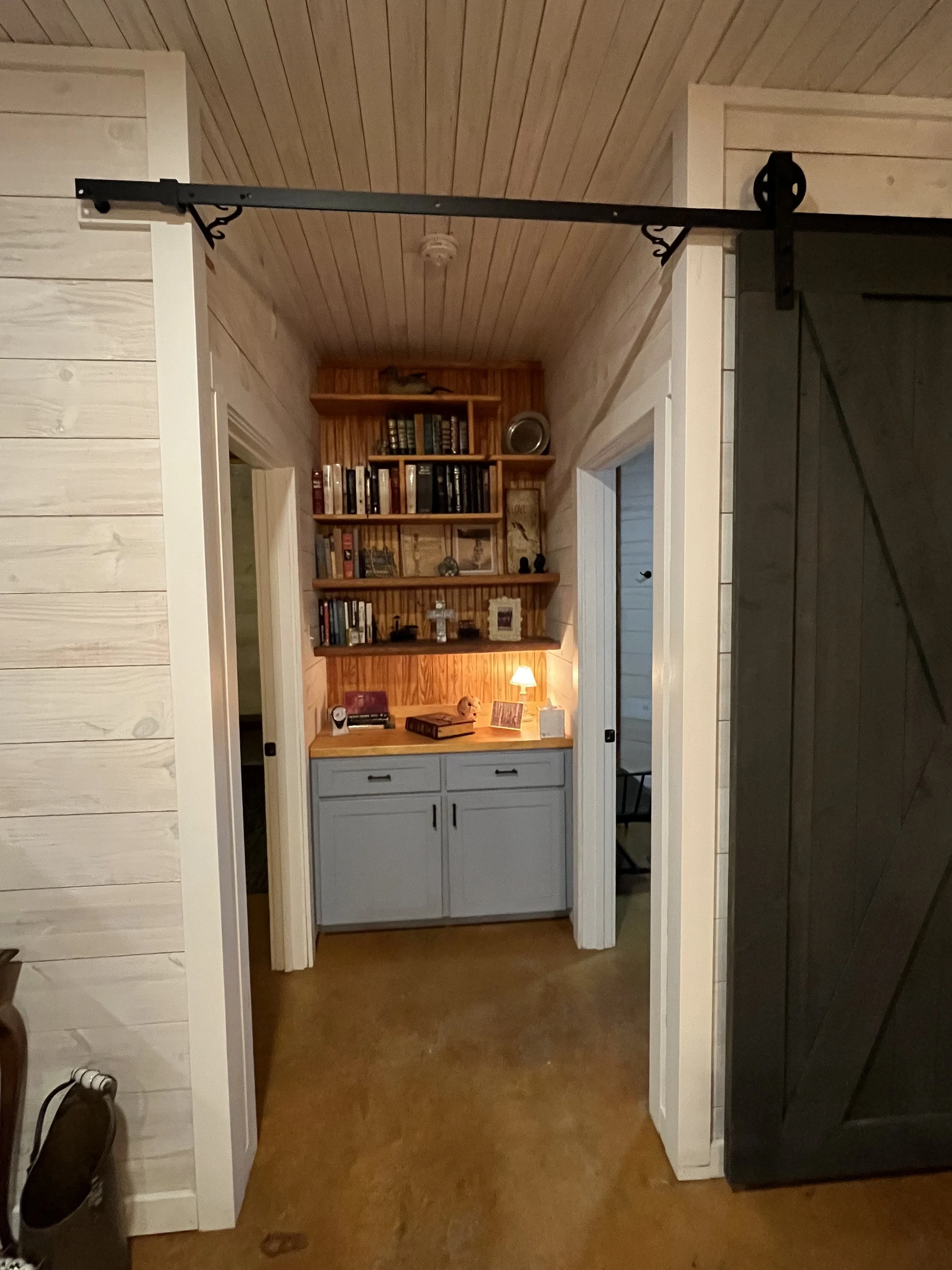 A built-in bookshelf with decorative items and books, a small lamp on the cabinet below, and a doorway on each side, all in a cozy, wood-paneled room.