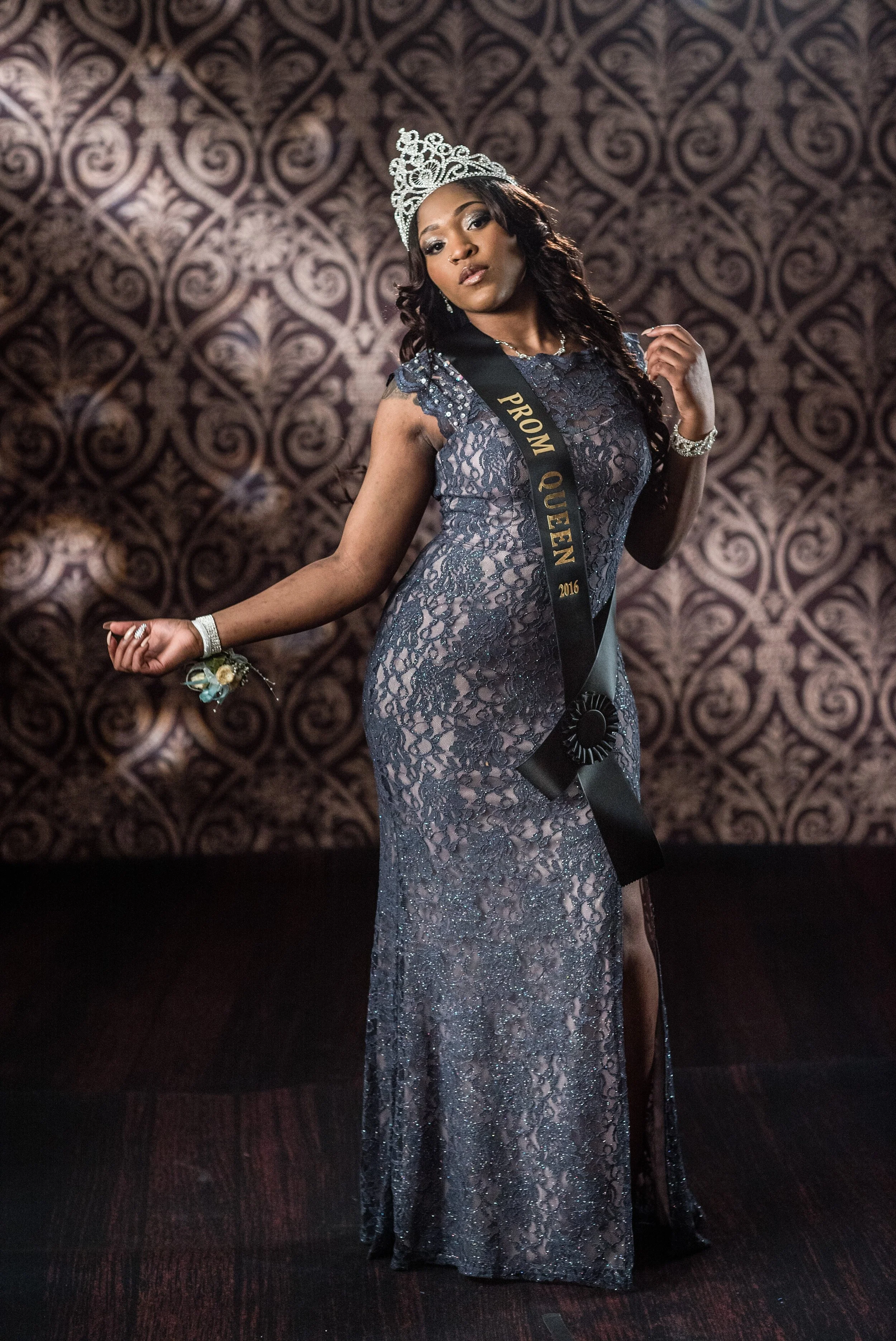 Flint Prom 2016 Woman wearing a crown, sash, and gown, with a crown and sash indicating she won Miss Queen 2016, posing confidently in front of a patterned background.