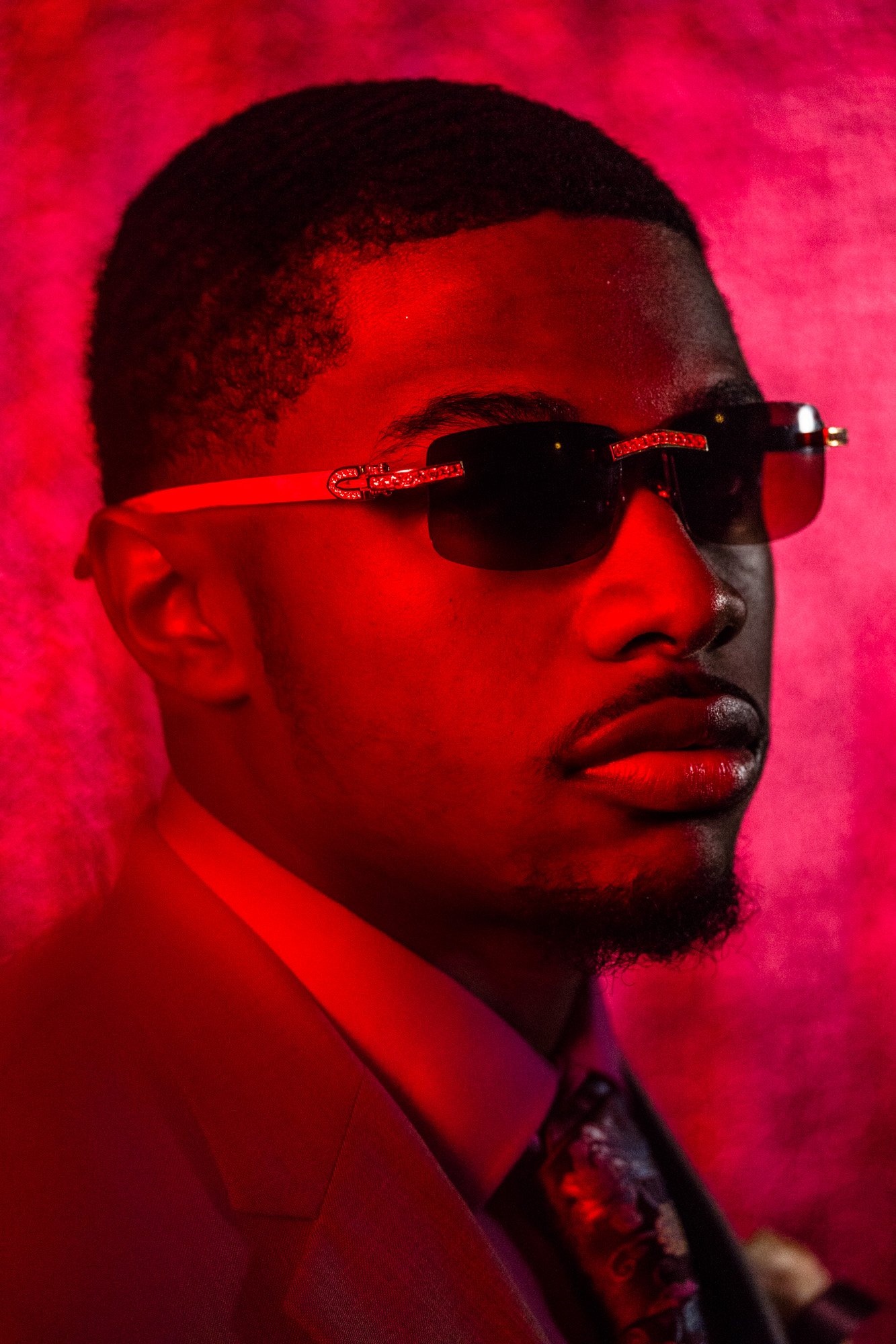 Portrait of a man with sunglasses, wearing a suit and tie, against a pink background from Flint Prom 2018