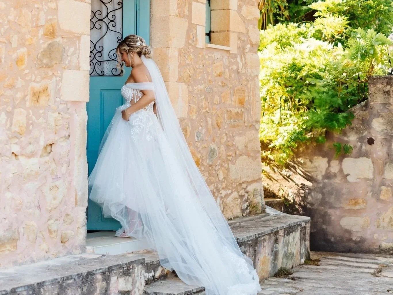 Bride walking into a traditional Mediterranean stone building with a pastel blue door.