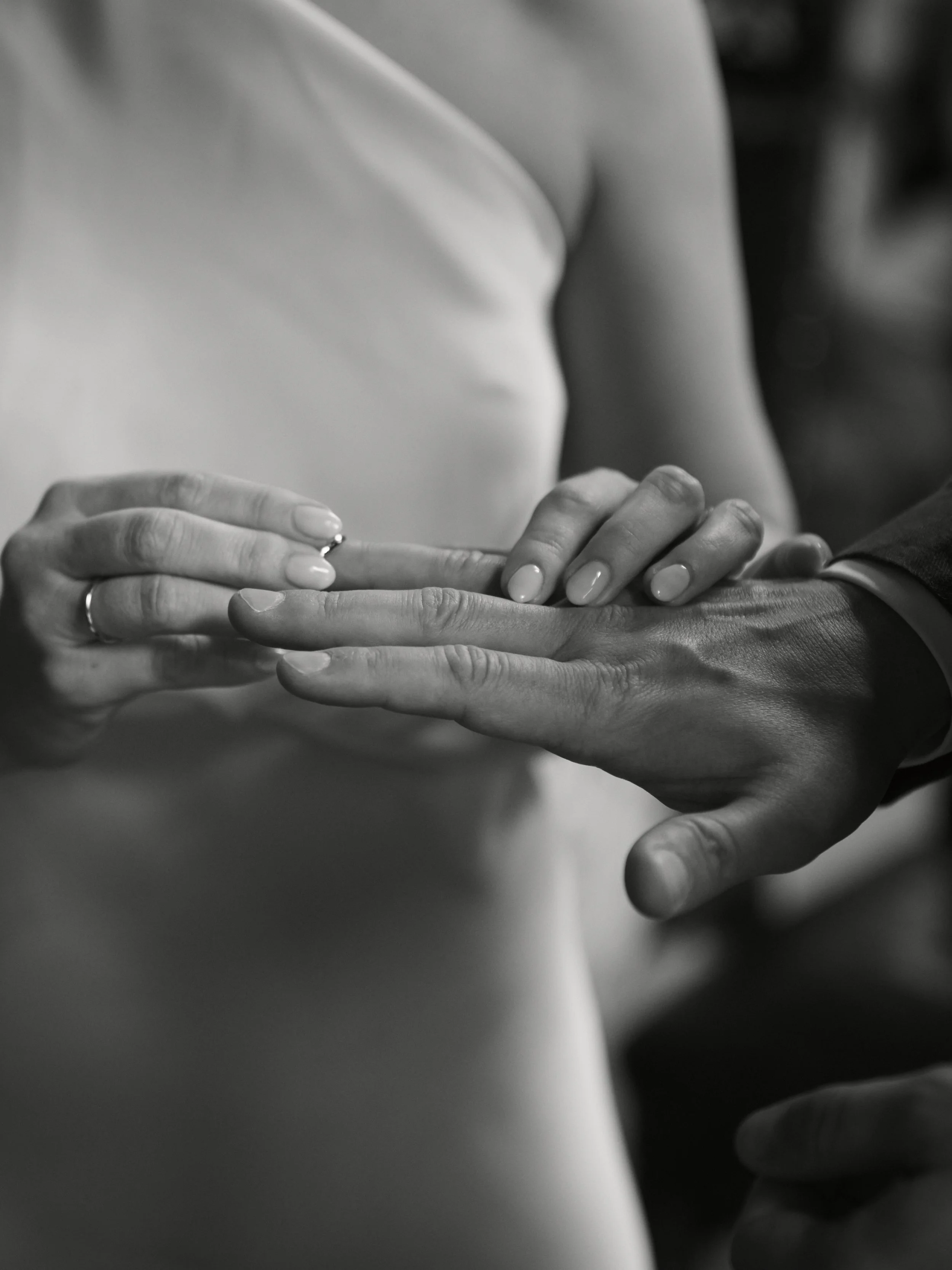 Die Braut steckt ihrem Bräutigam den Ring an den Finger während der Trauung in der Kirche. Schwarz-weiß Foto.