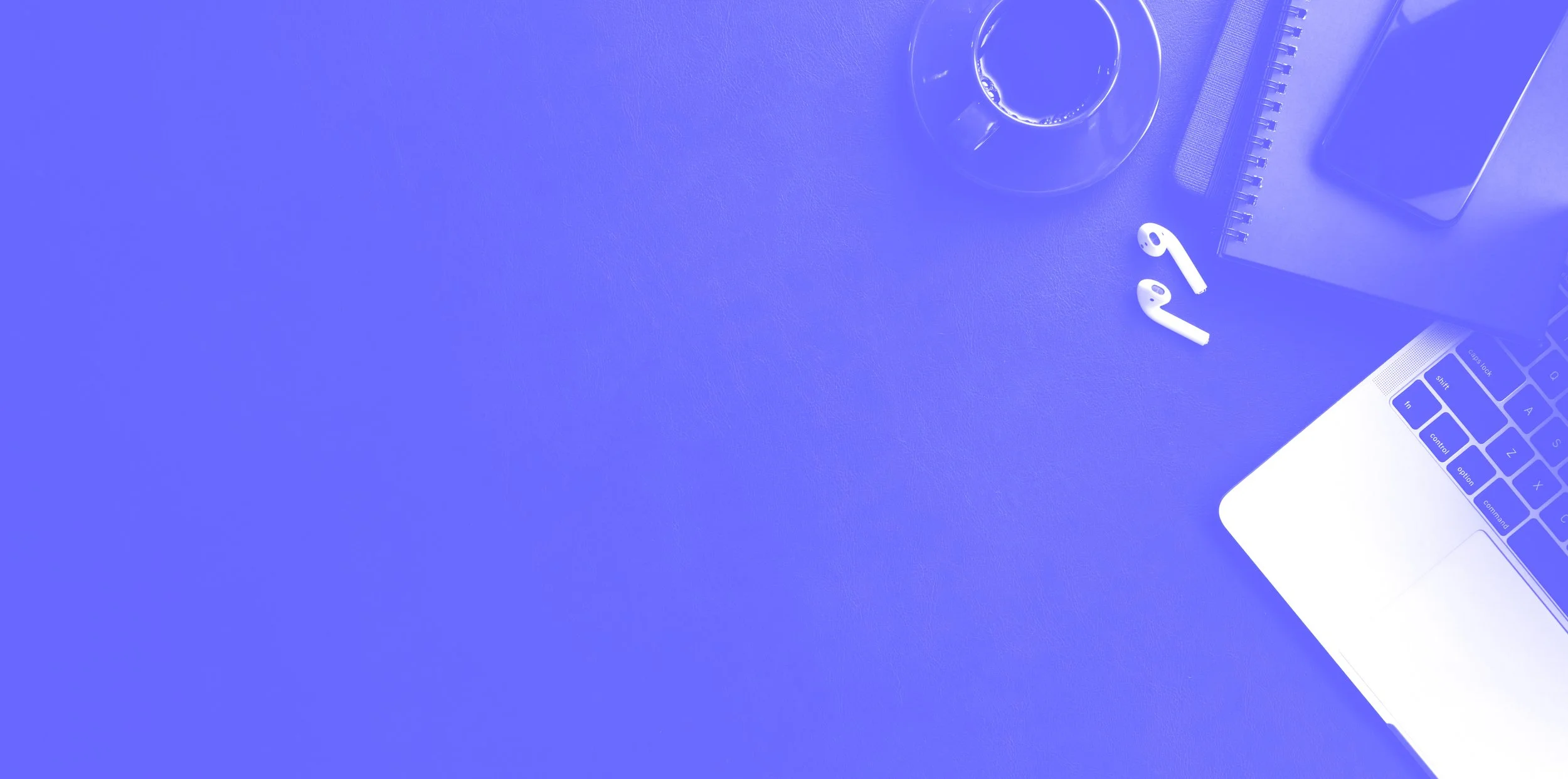 Overhead view of a workspace with a laptop, wireless earbuds, a glass of water, a notebook, a smartphone, and a pen on a purple surface.