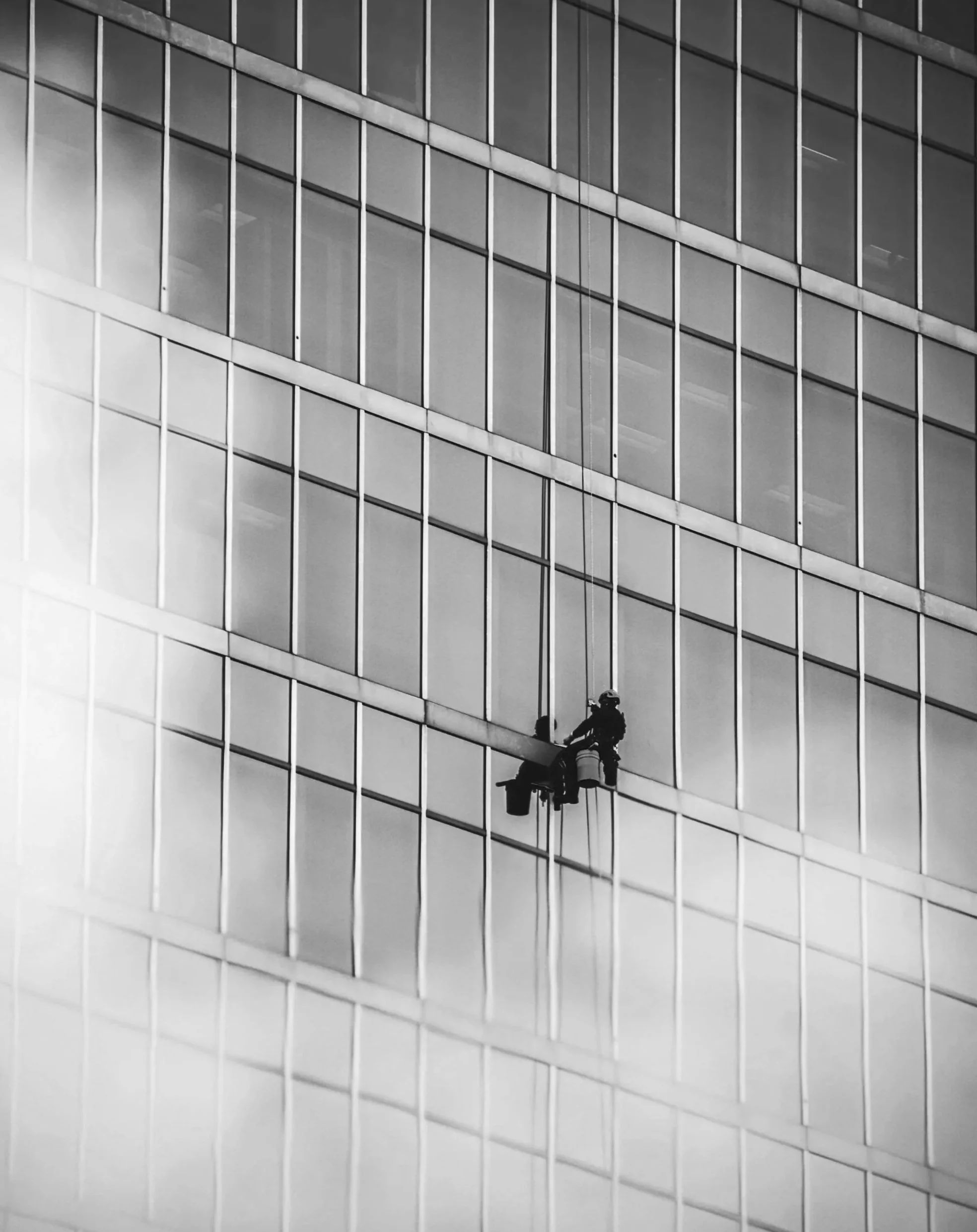 Zwei Arbeiter reinigen die Außenfassade eines modernen Glasgebäudes mit einer Hebebühne.