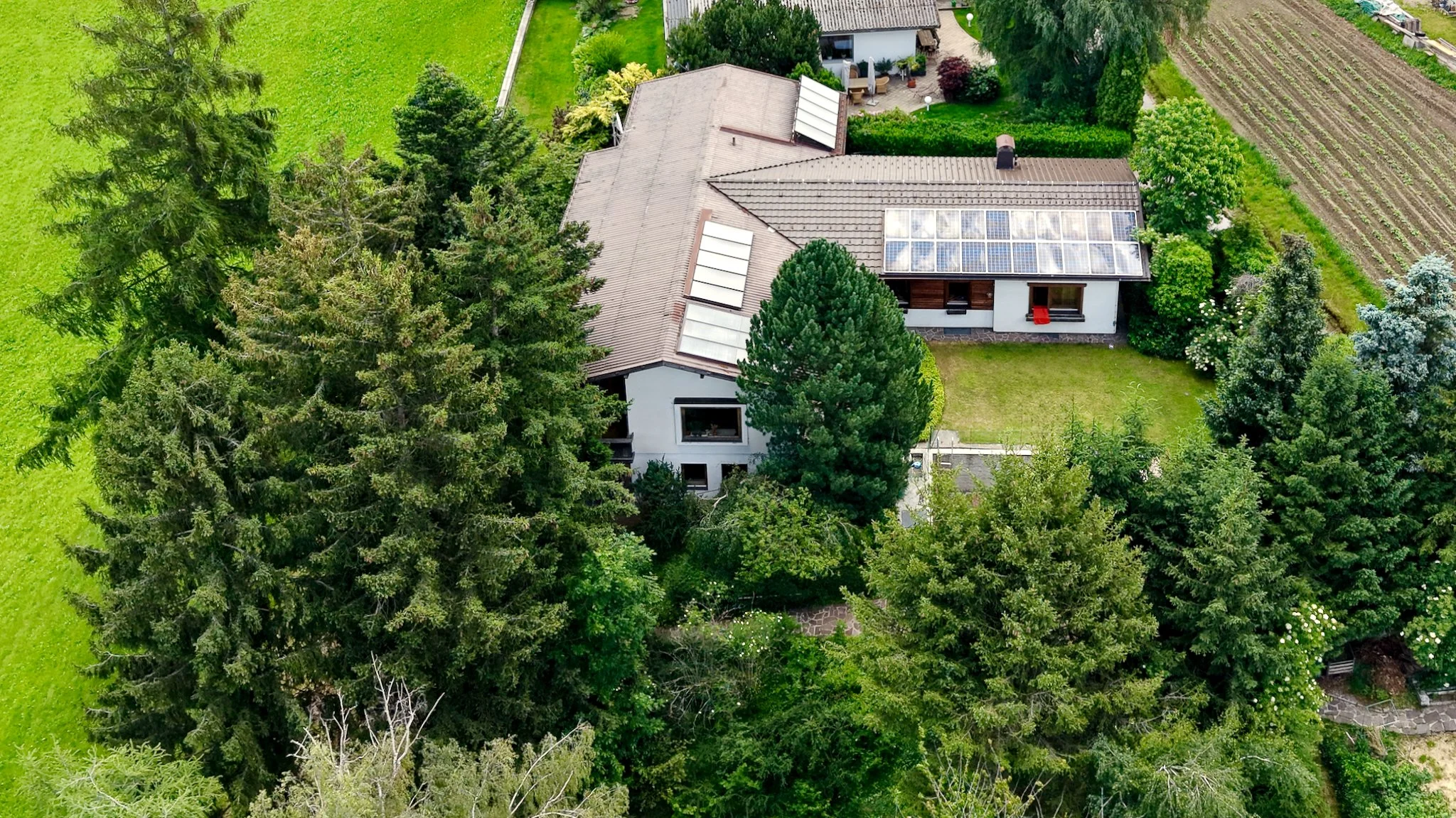 Vogelperspektive auf ein Haus mit Dachfenstern, umgeben von grünen Bäumen und Gärten in einer ländlichen Gegend.