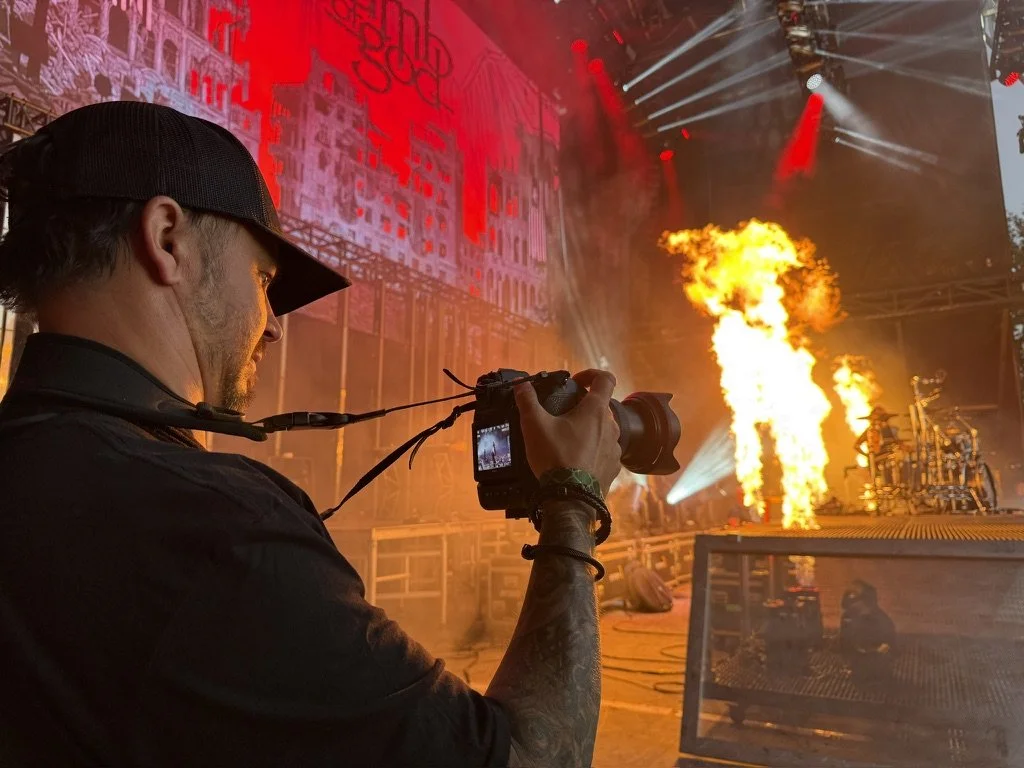 A photographer takes pictures of a stage with pyrotechnics showing flames and bright lights during a live concert.