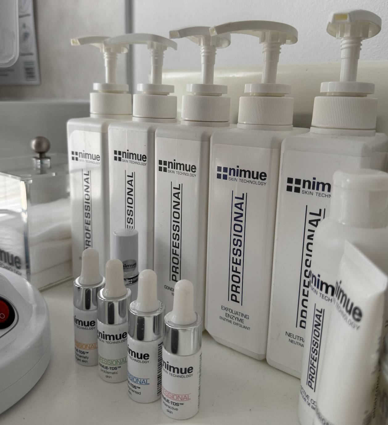 Collection of Nimue skincare products including large bottles labeled 'Professional', smaller bottles, and dropper bottles, arranged on a white trolley surface.