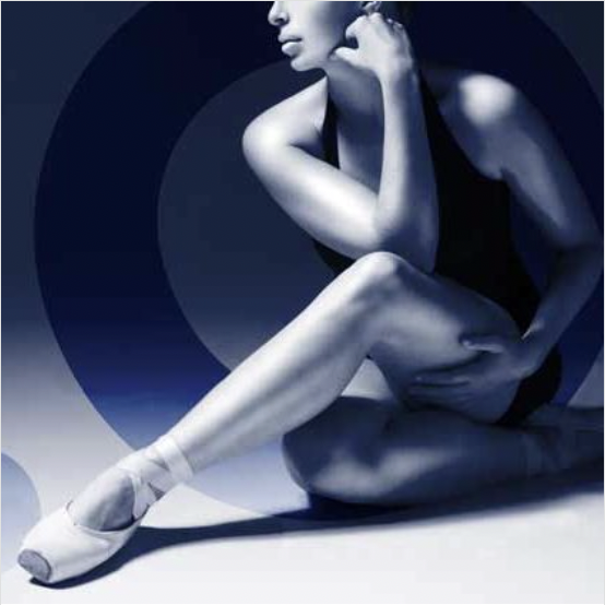 A ballerina sitting on the floor with one leg extended and the other bent, wearing ballet shoes, in a monochromatic setting.