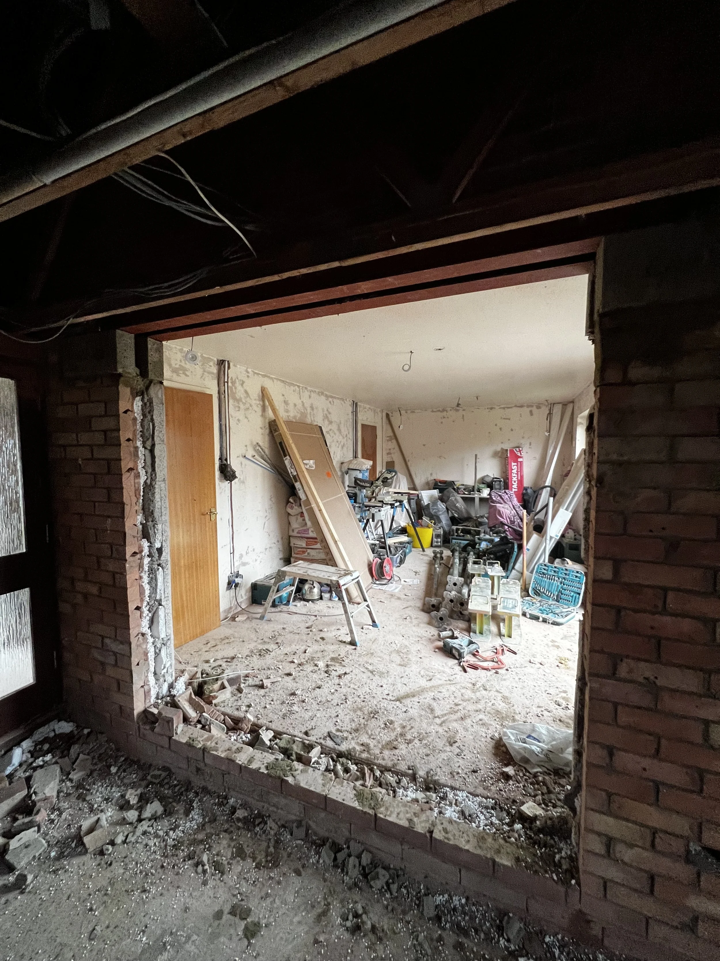 View of a room under construction or renovation with exposed brick walls and scattered construction tools and materials, including a saw, drill, ladder, and boxes.
