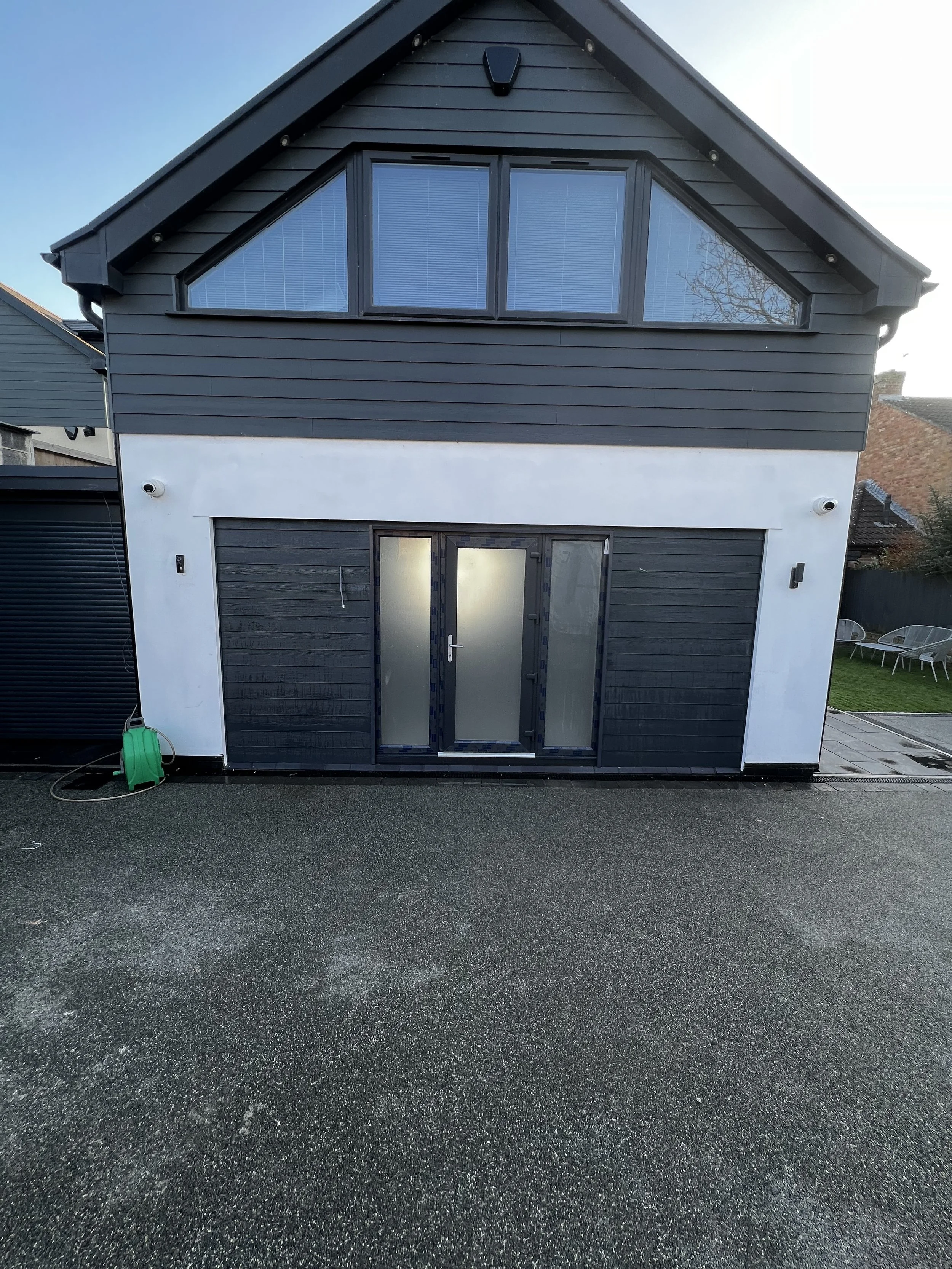 Exterior of a modern two-story house with black siding and large upper windows, sliding glass door on the ground level, and driveway in front.