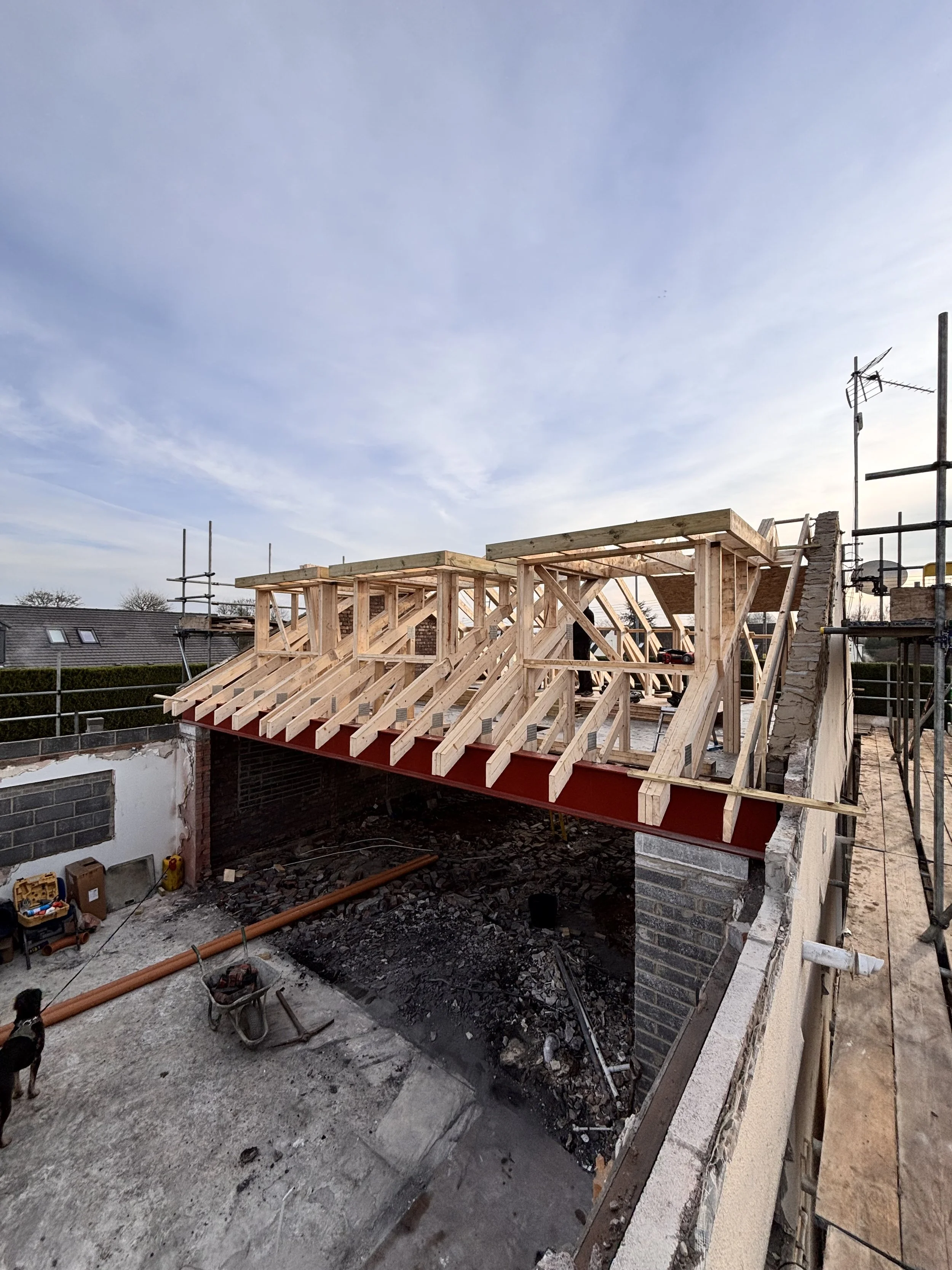 Construction site with wooden framework for a building or bridge, with scaffolding on the side and an open space underneath, during daytime with a clear sky.