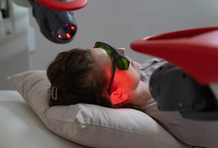 A patient relaxes while red laser light is gently directed at the ear. This non-invasive therapy stimulates inner ear cells to help reduce tinnitus, hearing loss, and vertigo.