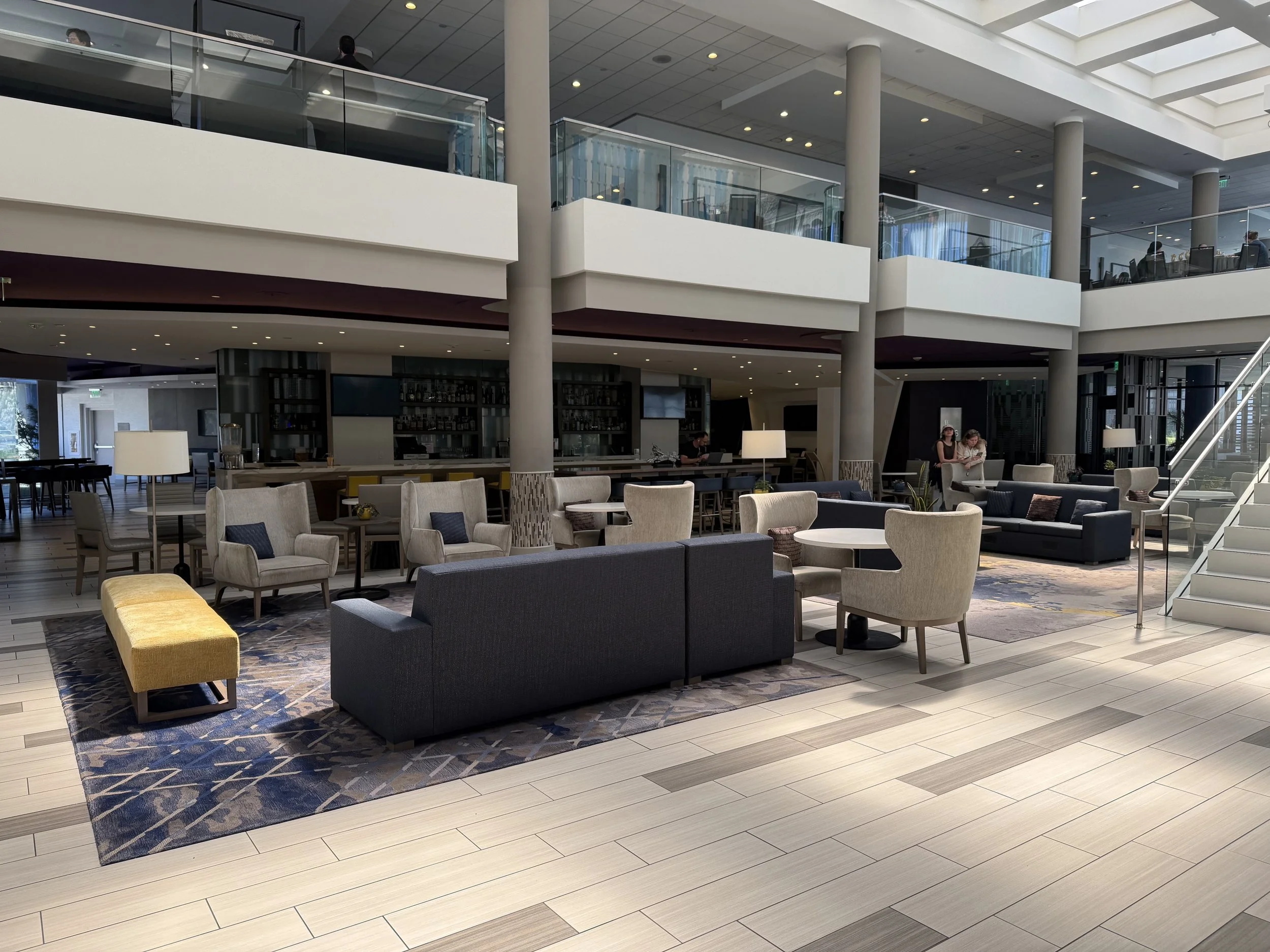 Modern hotel lobby with seating area, second-floor balcony, and staircase.