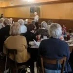 Group of elderly people sitting and listening to a speaker in a community event or meeting.