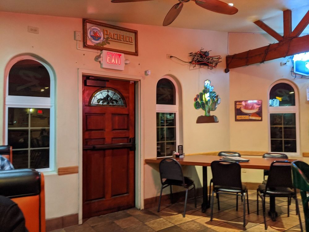 Interior of a restaurant or bar with a wooden door, several windows, and various decorations on the walls, including a sign that reads 'Pacifico' and a neon 'Exit' sign.