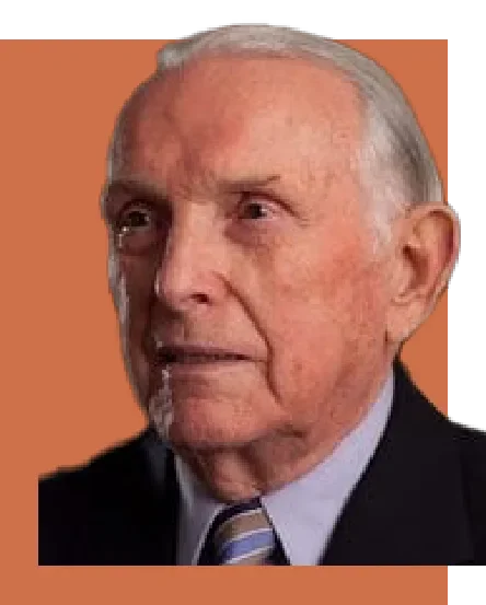 Close-up of an elderly man with gray hair, wearing a suit and striped tie, against an orange background.