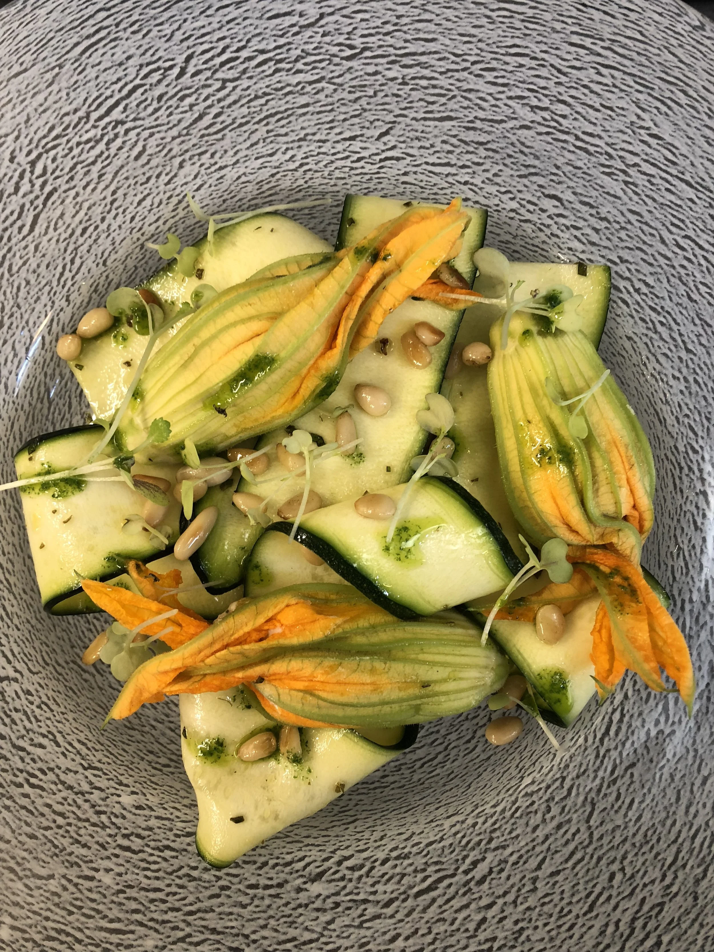 A bowl of sliced zucchini garnished with small sprouts and pumpkin seeds.