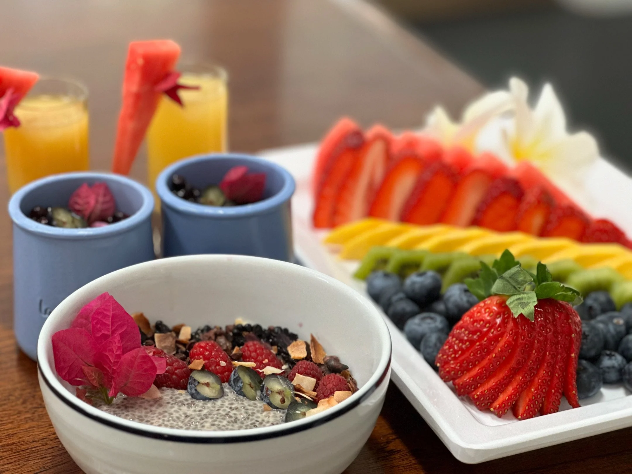 Assorted bowls of berries, a fruit platter with sliced strawberries, kiwis, mangos, and strawberries, and glasses of orange juice with watermelon garnishes.