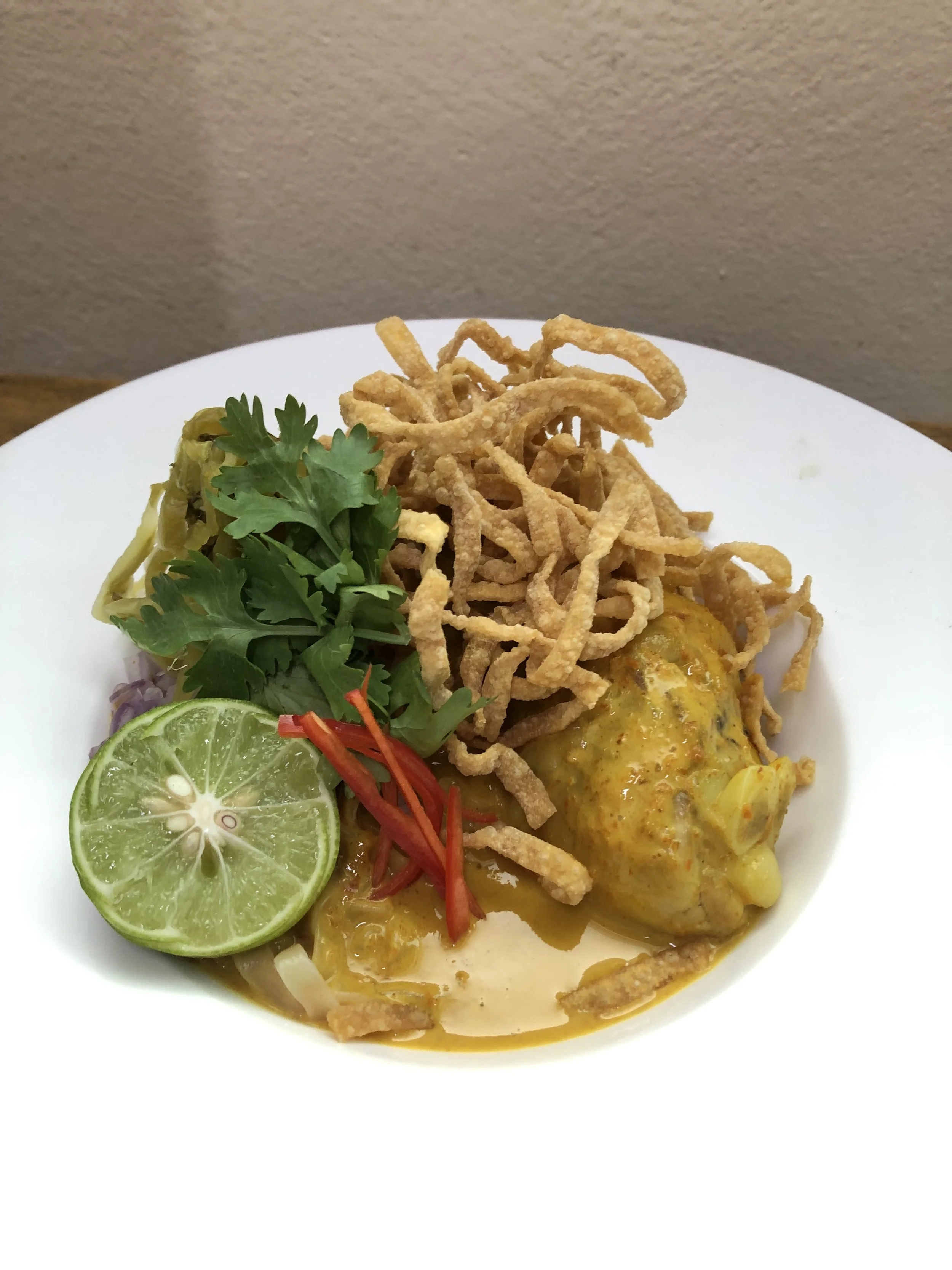 Plate of Thai curry with fried noodles, lime, cilantro, red chili, and vegetables.